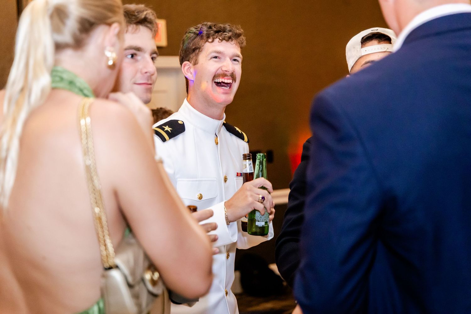 Wedding guests socializing and laughing during an evening reception with warm lighting.