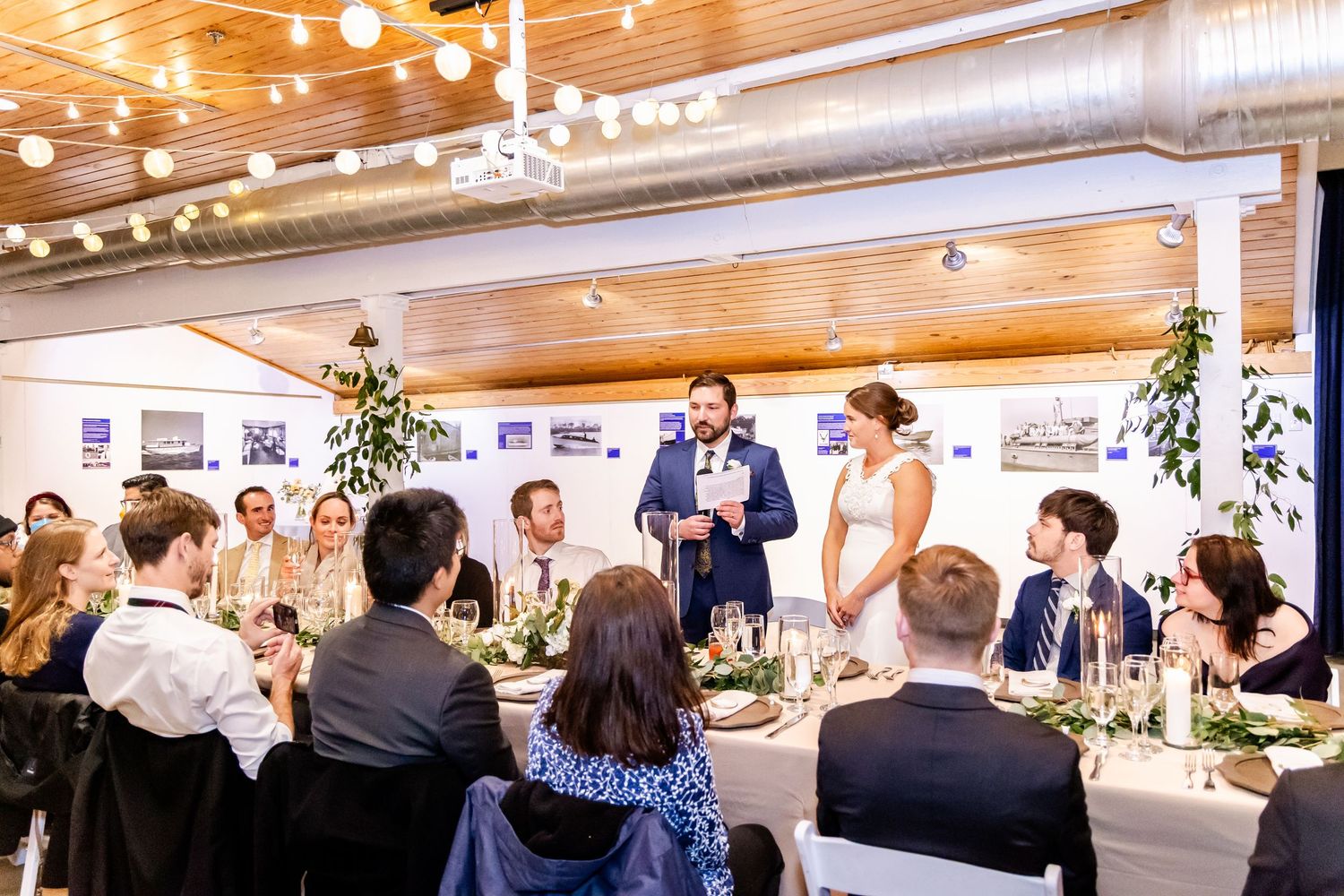 Wedding reception toast with groom speaking to elegantly dressed guests at candlelit tables in a modern venue.
