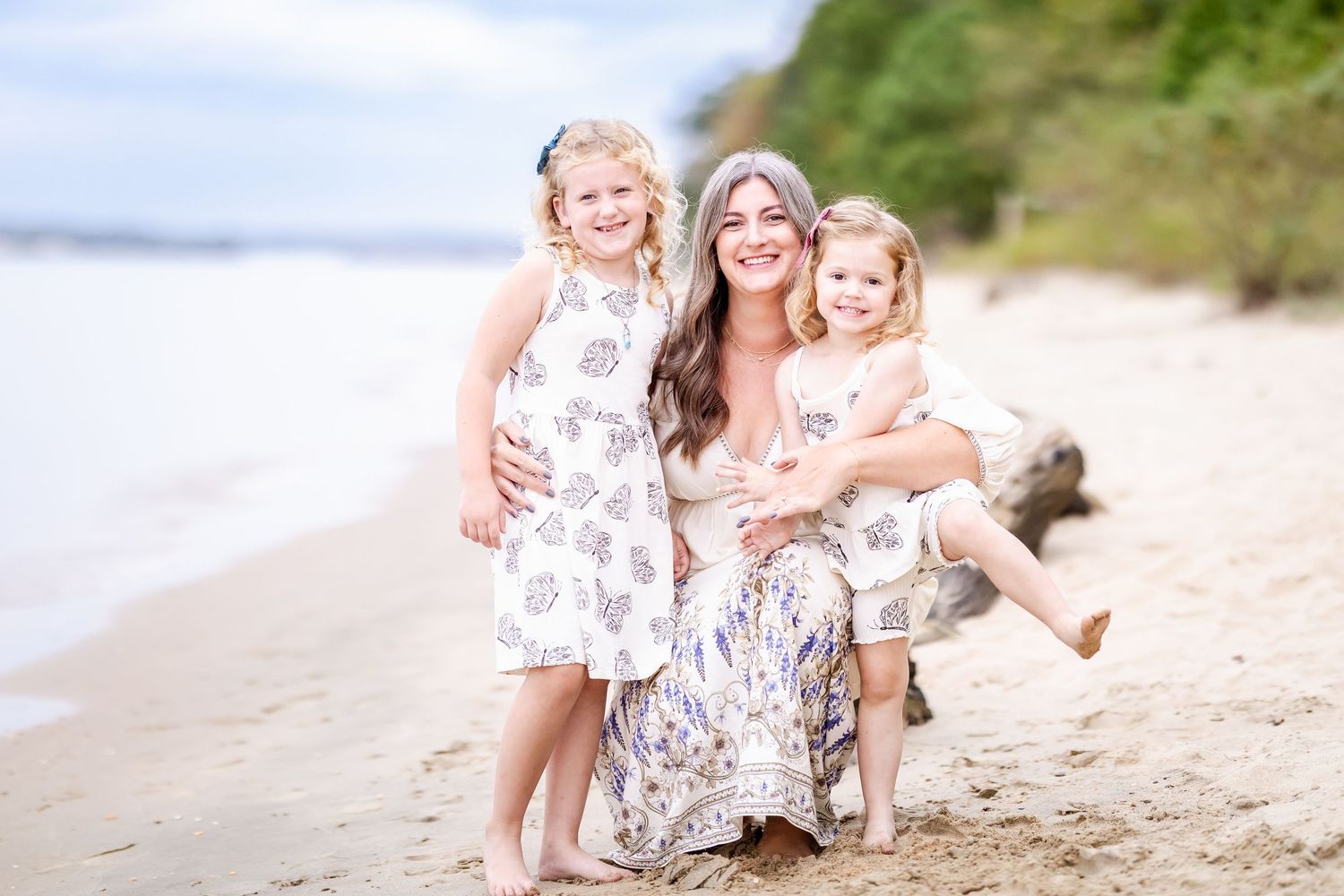 Family wearing white outfits sits together on a sandy beach during sunset photo session.