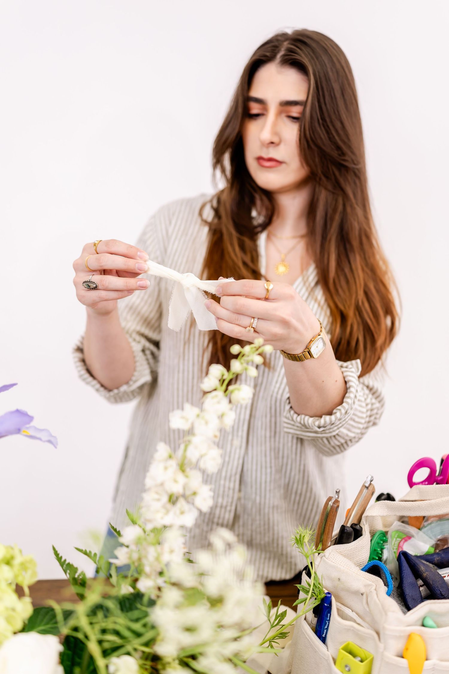 Young female florist arranging white flowers at a worktable with tools and supplies in a bright studio.
