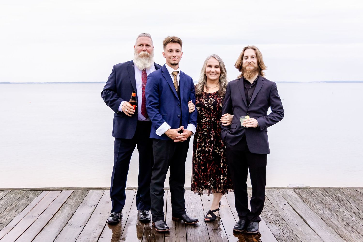 Wedding party members posing together on a wooden deck overlooking the water.