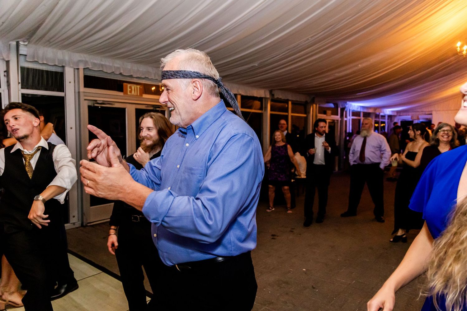 Evening wedding reception with guests dancing under warm lighting in a tented outdoor space.