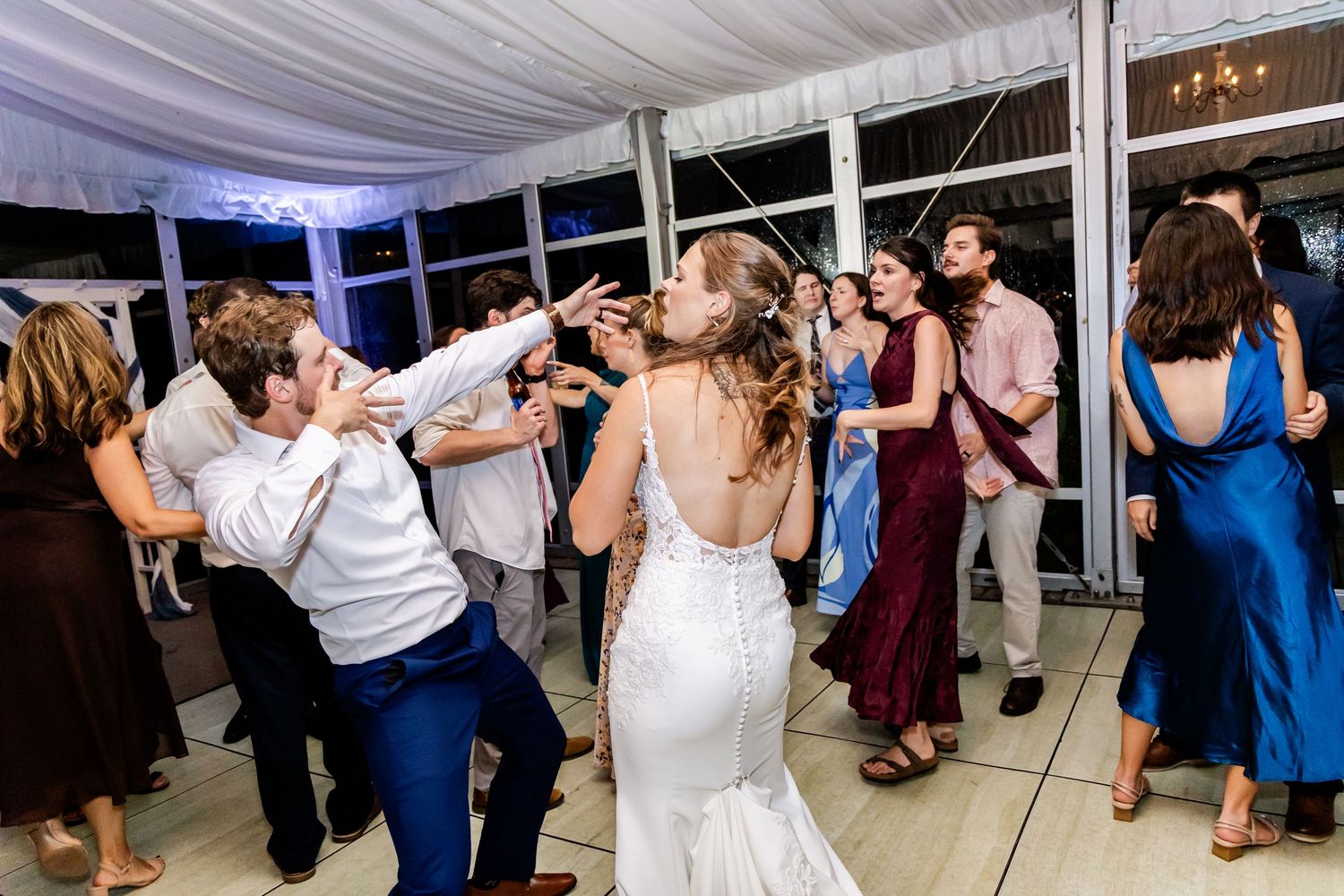 Wide view of wedding reception dance floor with guests celebrating under elegant white tent.