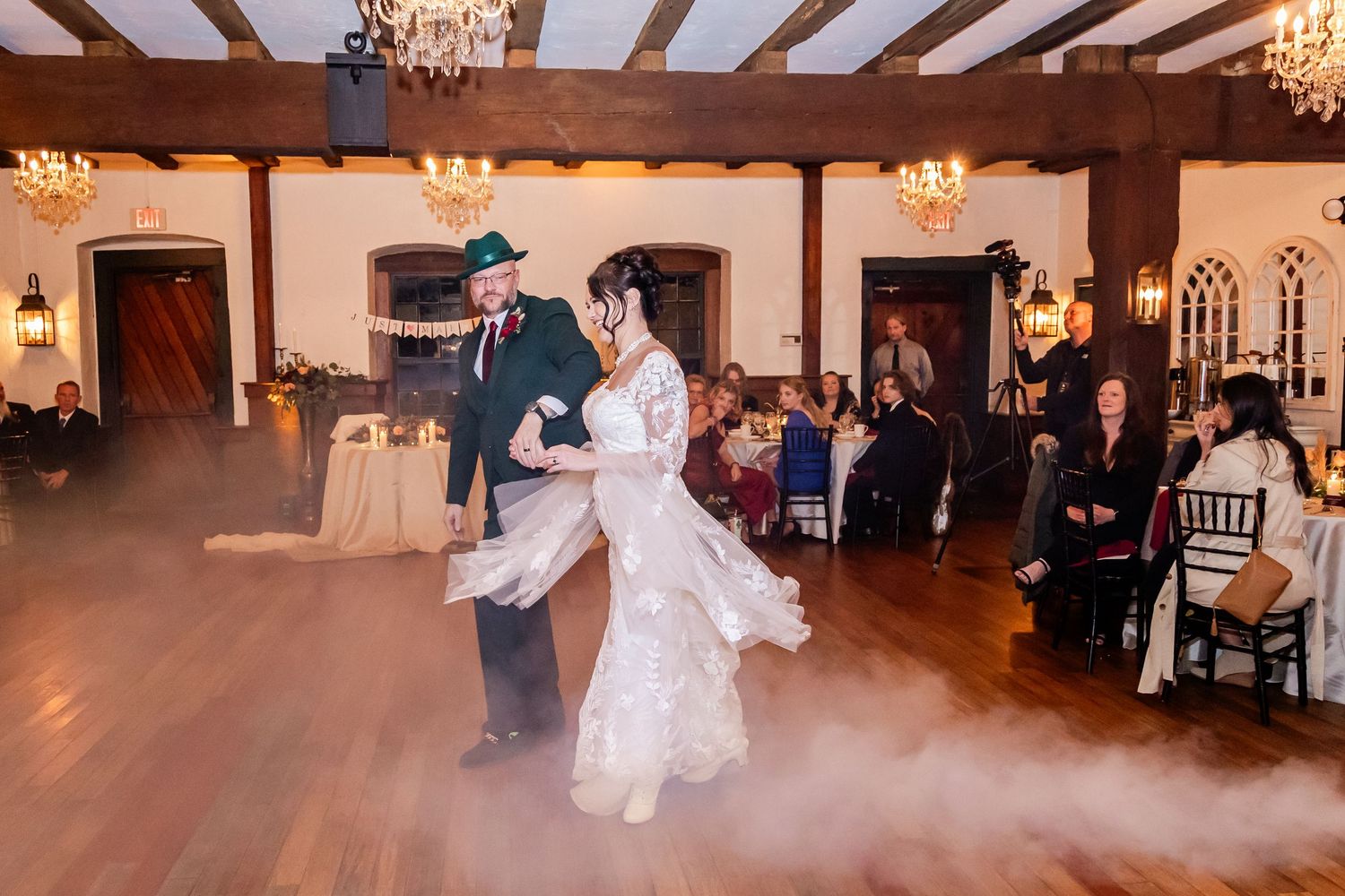 Newlyweds dancing in a grand ballroom with exposed wooden beams and chandeliers.