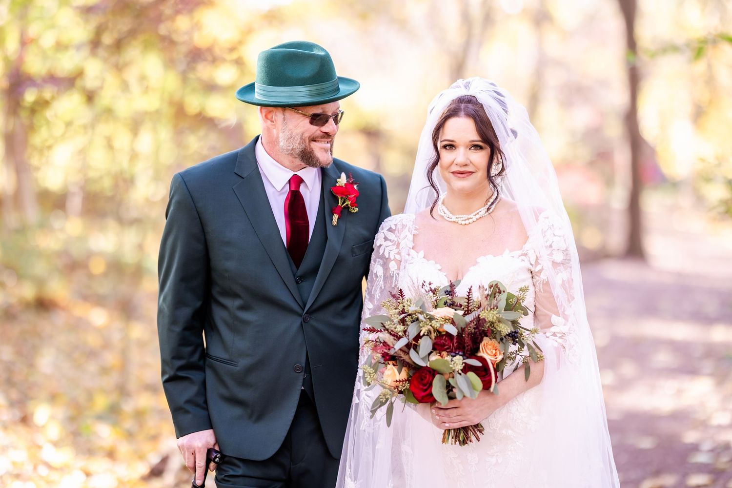 A couple poses together during an autumn wedding ceremony in a wooded forest setting with warm golden light.