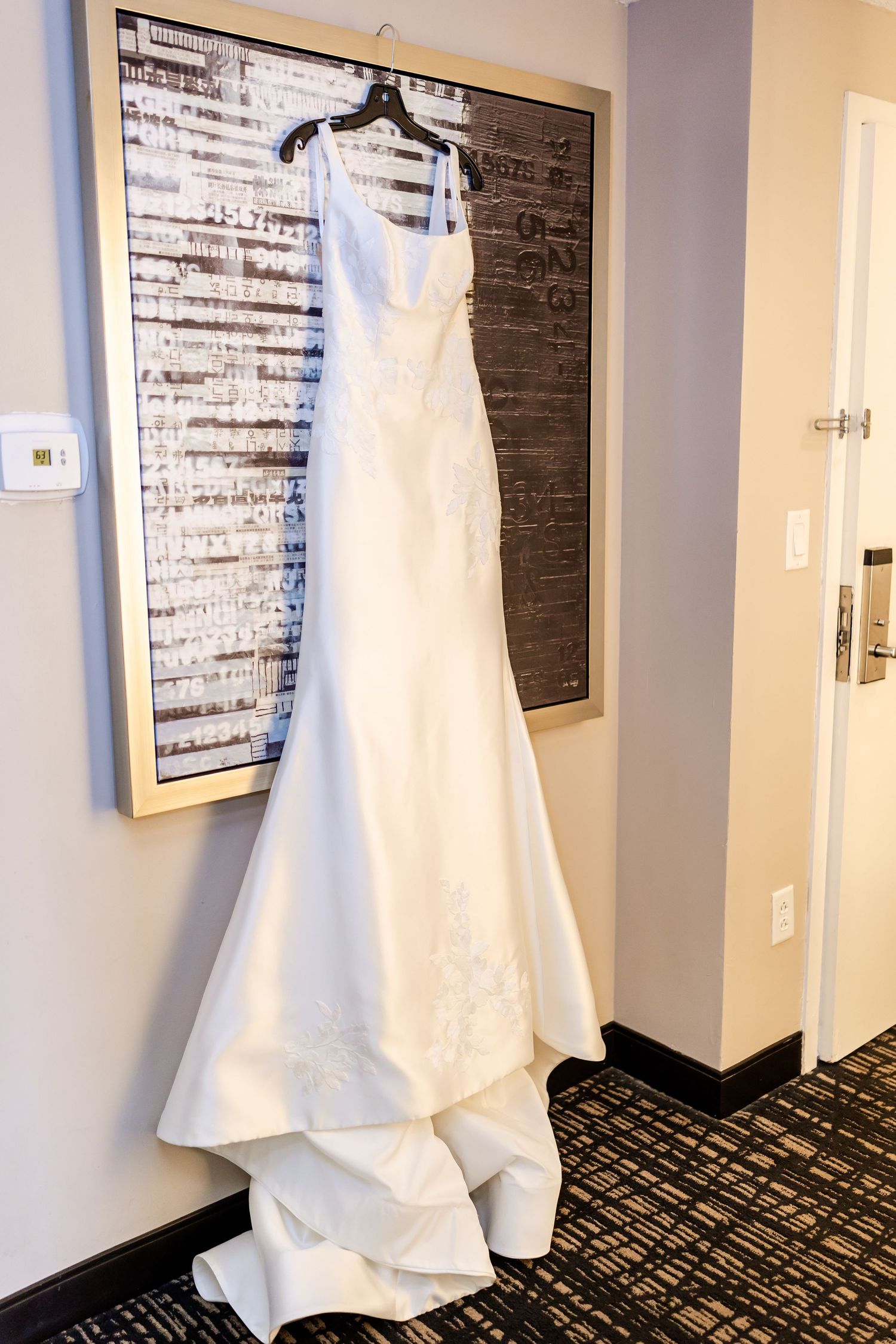 White wedding dresses hanging on display in a hotel hallway with patterned carpet.