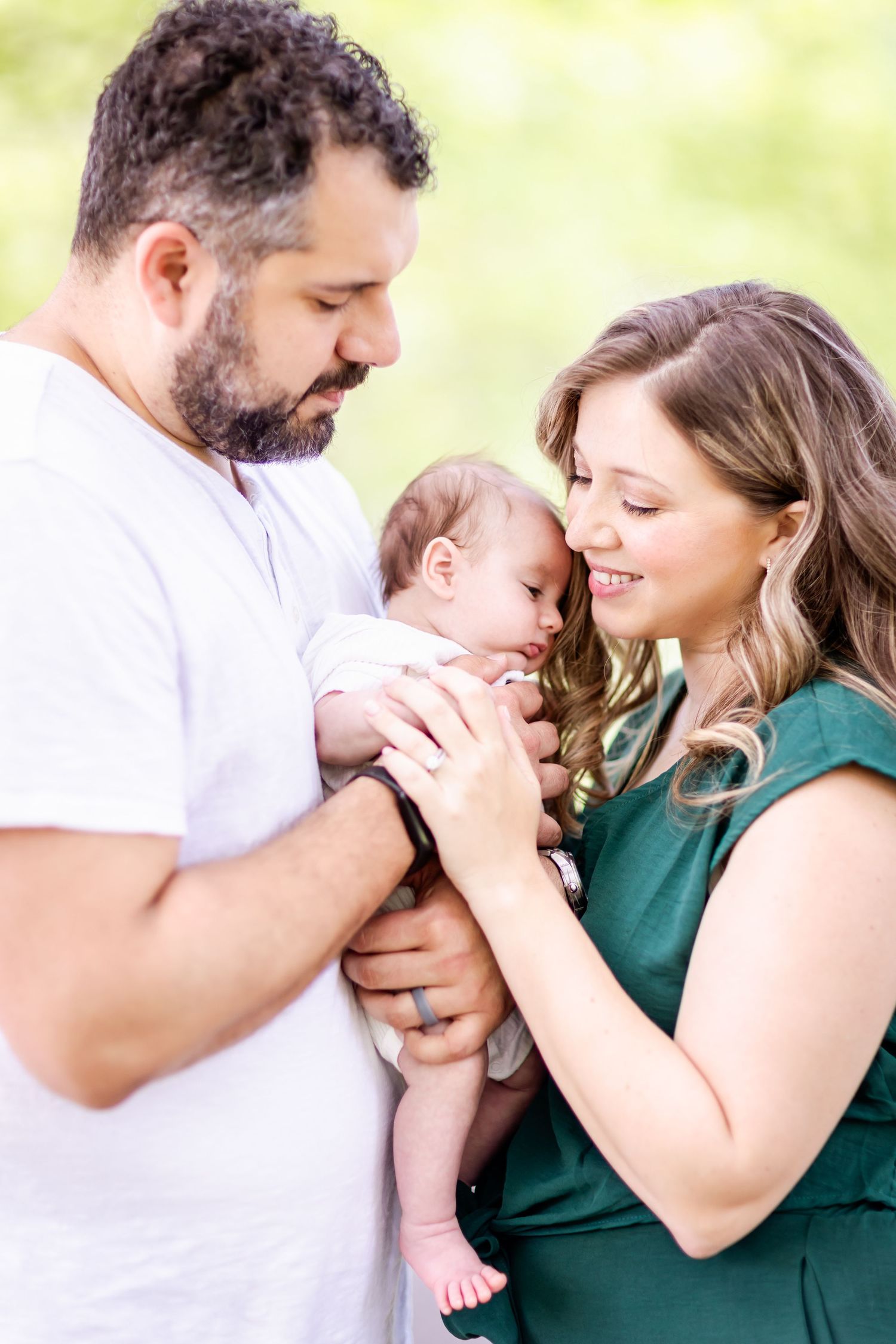 Parents lovingly embrace their newborn baby outdoors in a tender family moment.