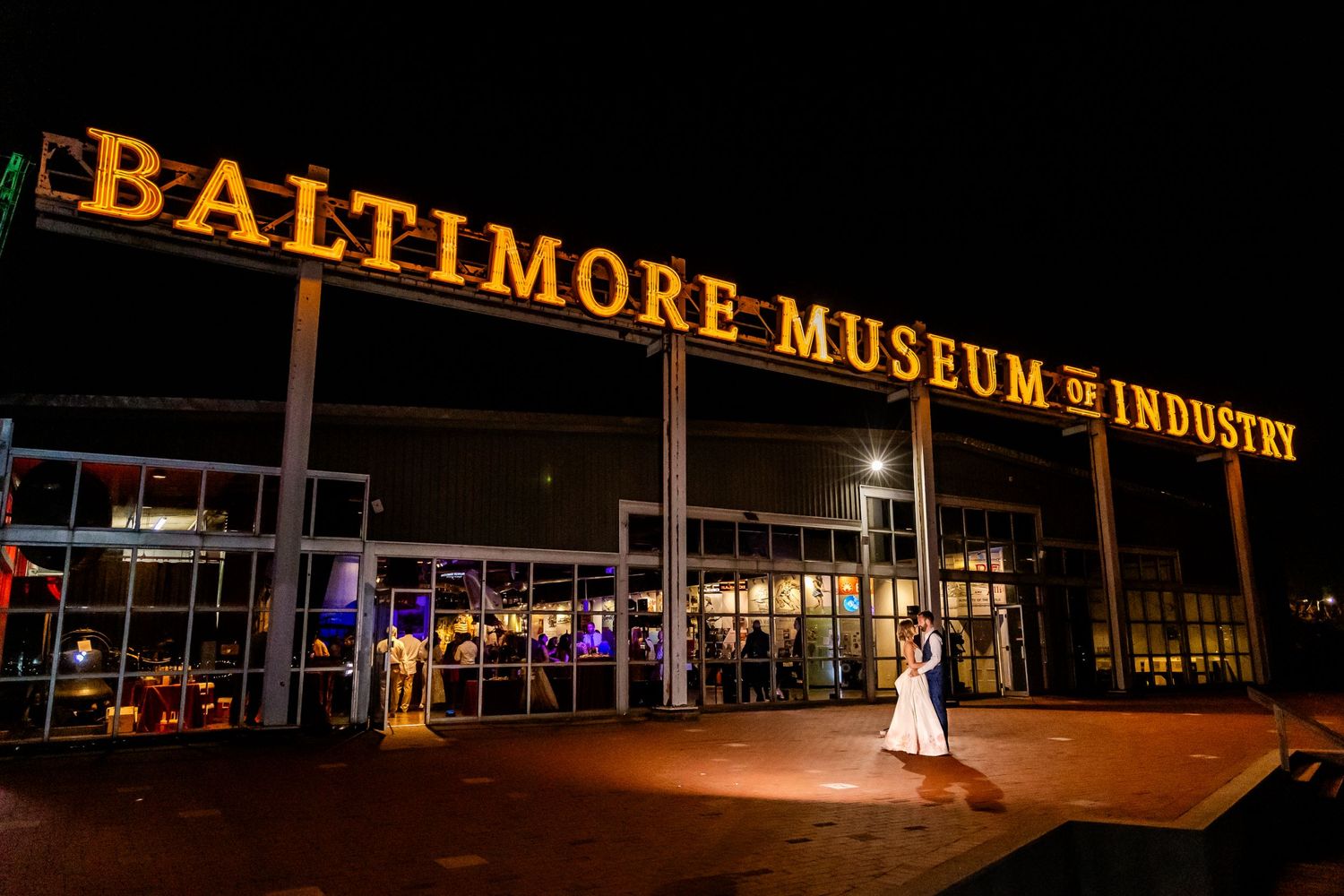 Wedding couple silhouetted against the illuminated Baltimore Museum of Industry building at night.