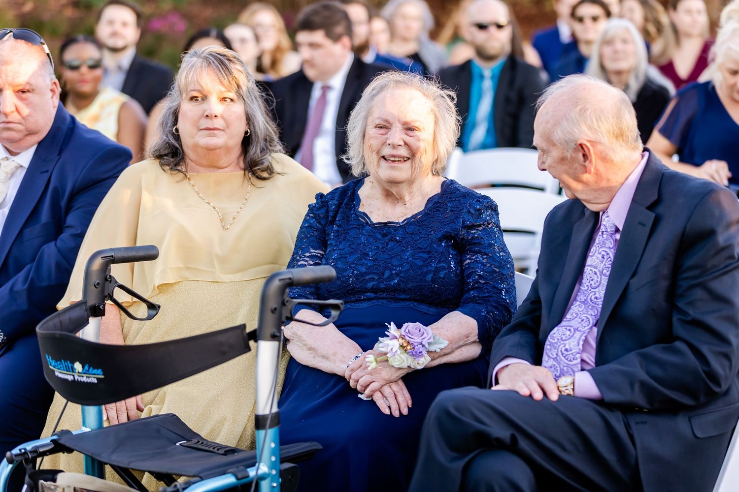 Wedding guests seated in formal attire at outdoor ceremony venue.