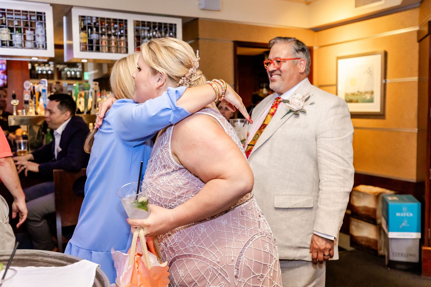 Guests share an emotional moment during a celebration at an indoor venue bar area.