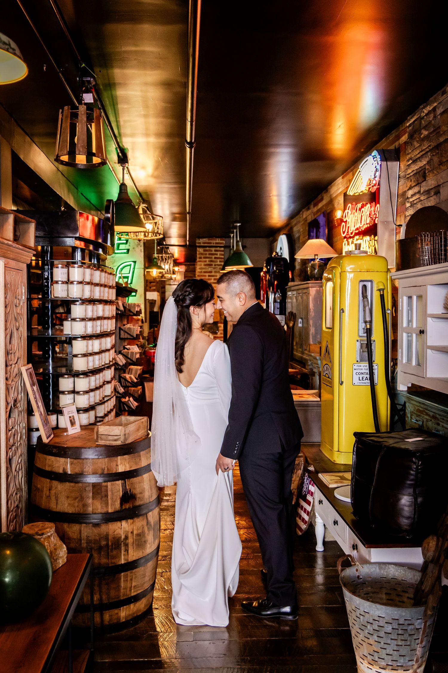 A newlywed couple embraces in a vintage-style bar with wooden barrels and neon signs.