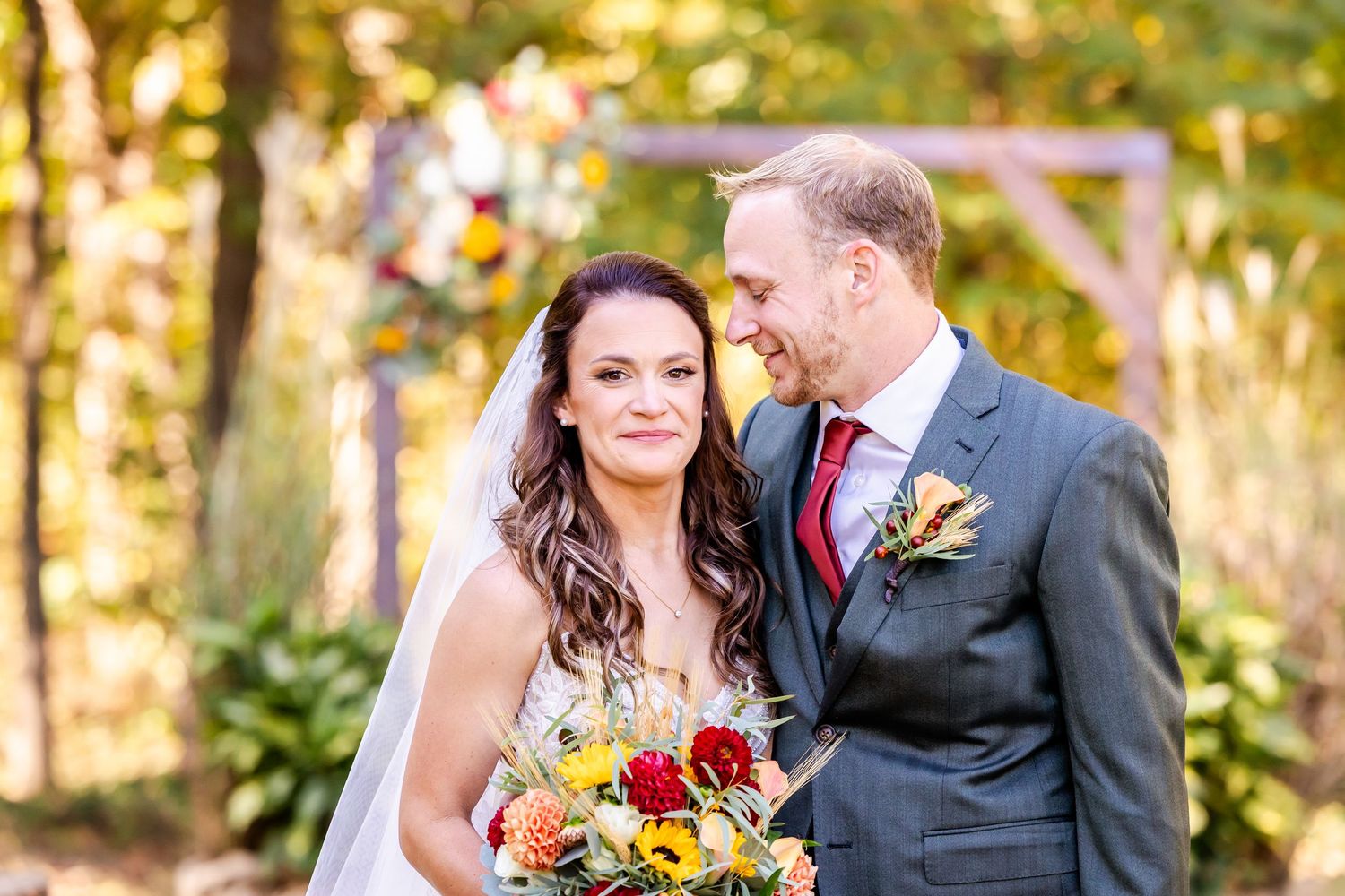 Wedding couple embraces in front of golden autumn foliage during sunset.