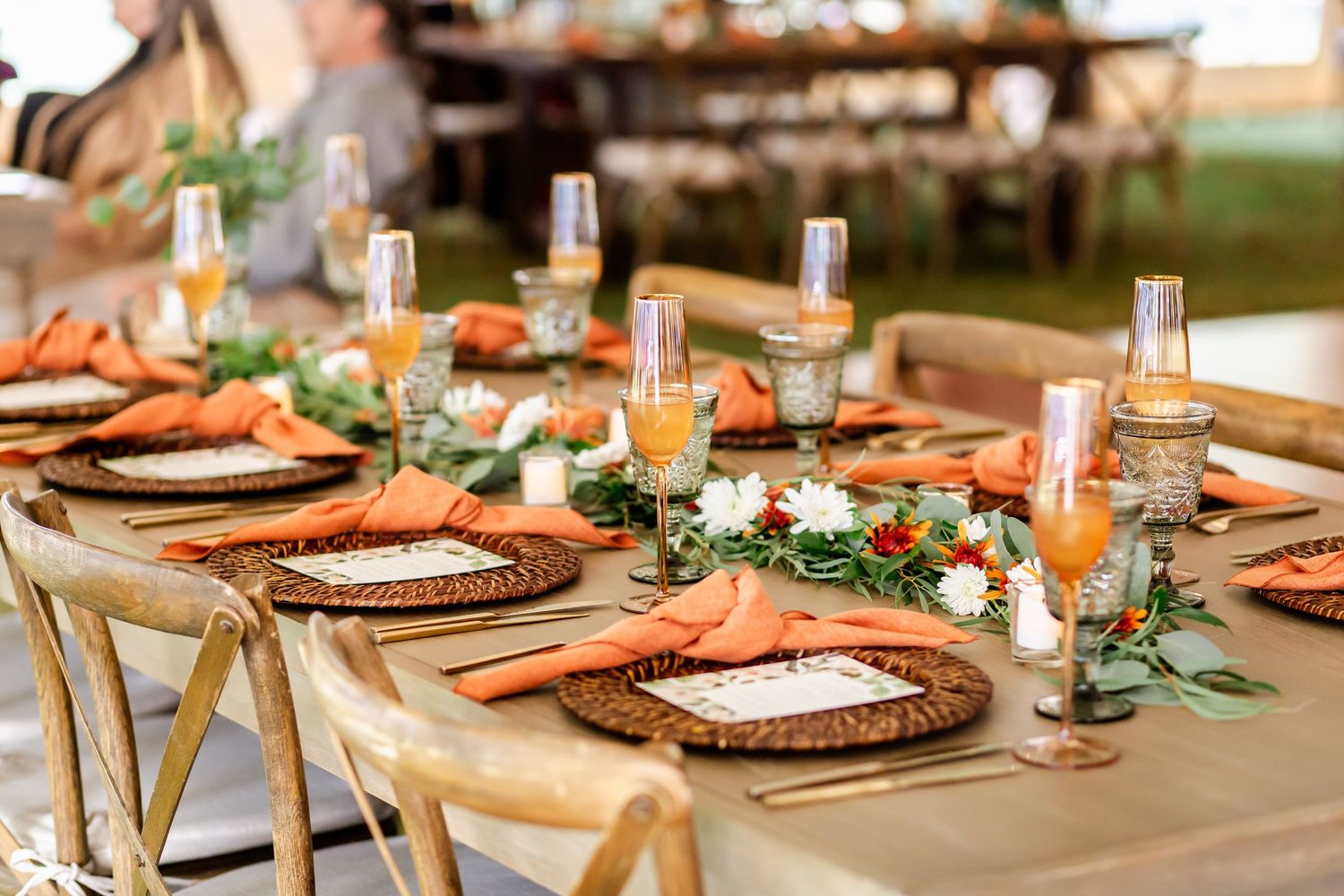 Rustic wedding reception tables decorated with orange chargers, greenery and wooden accents.