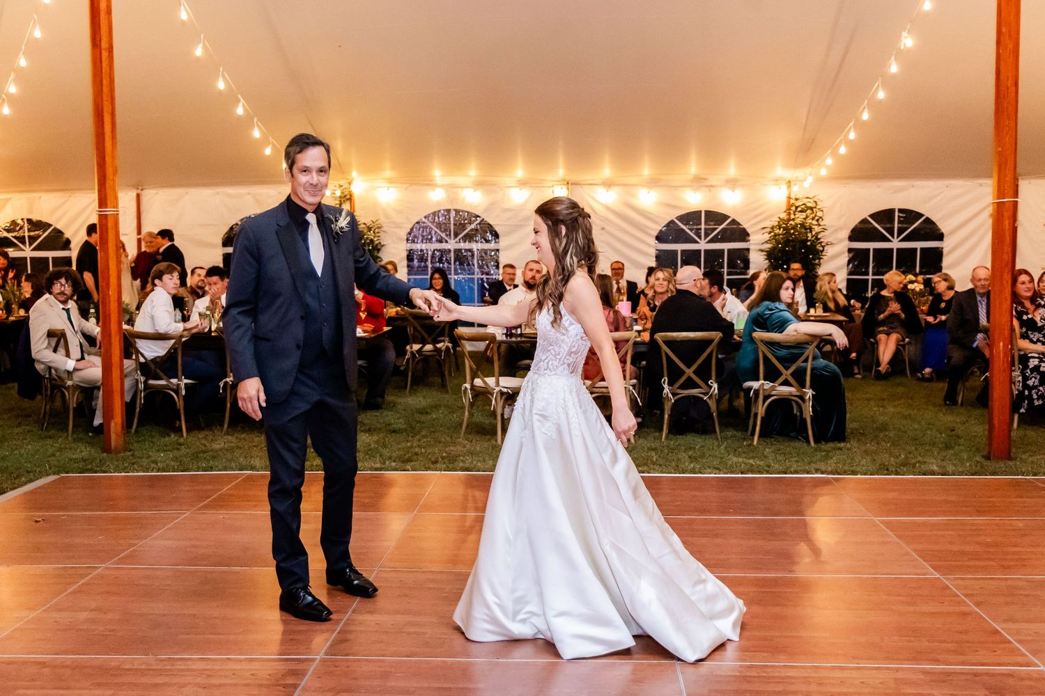 Newlyweds dance on wooden floor under string lights at their tented wedding reception.