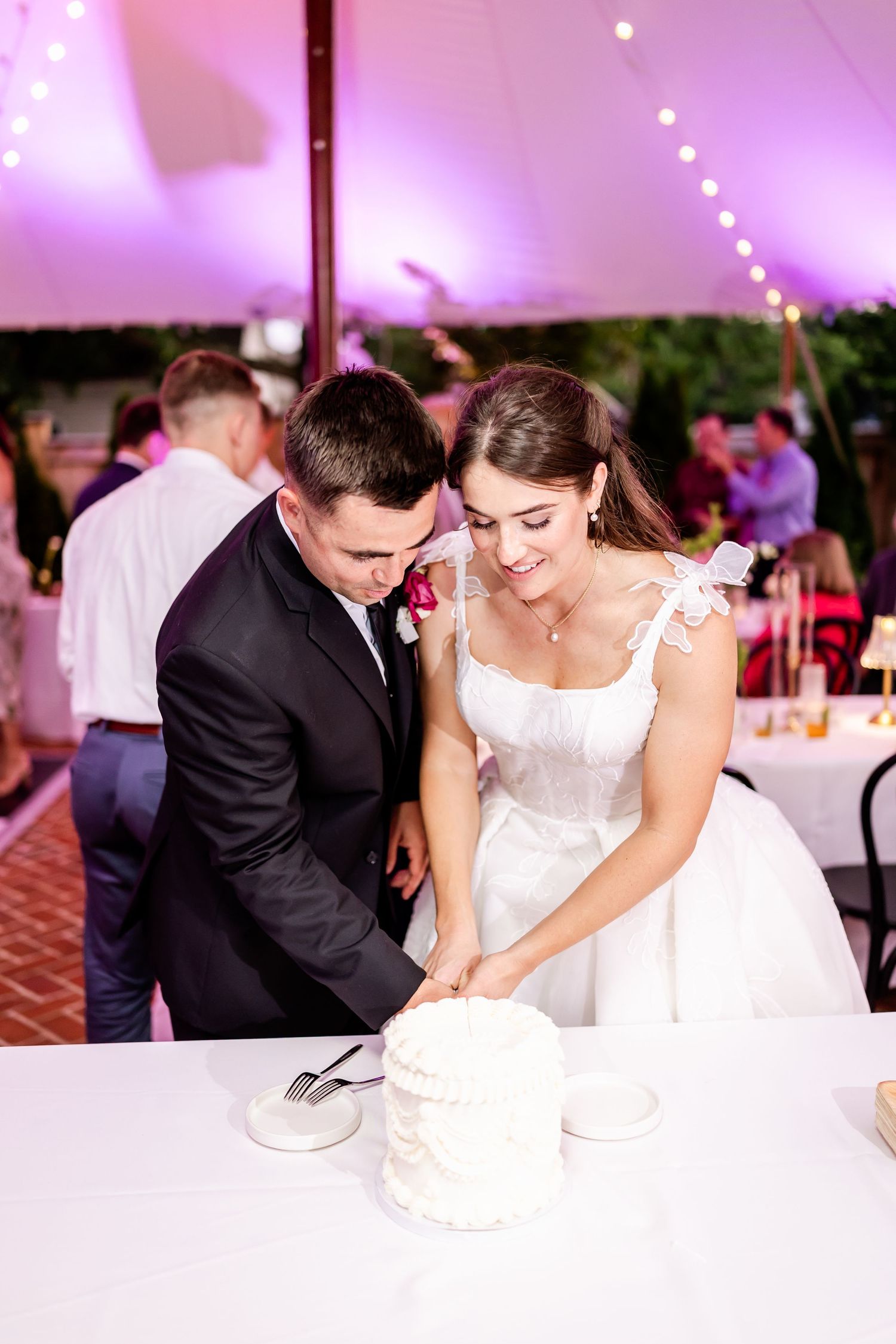 Couple shares a romantic moment cutting their wedding cake together under purple lighting at their reception.