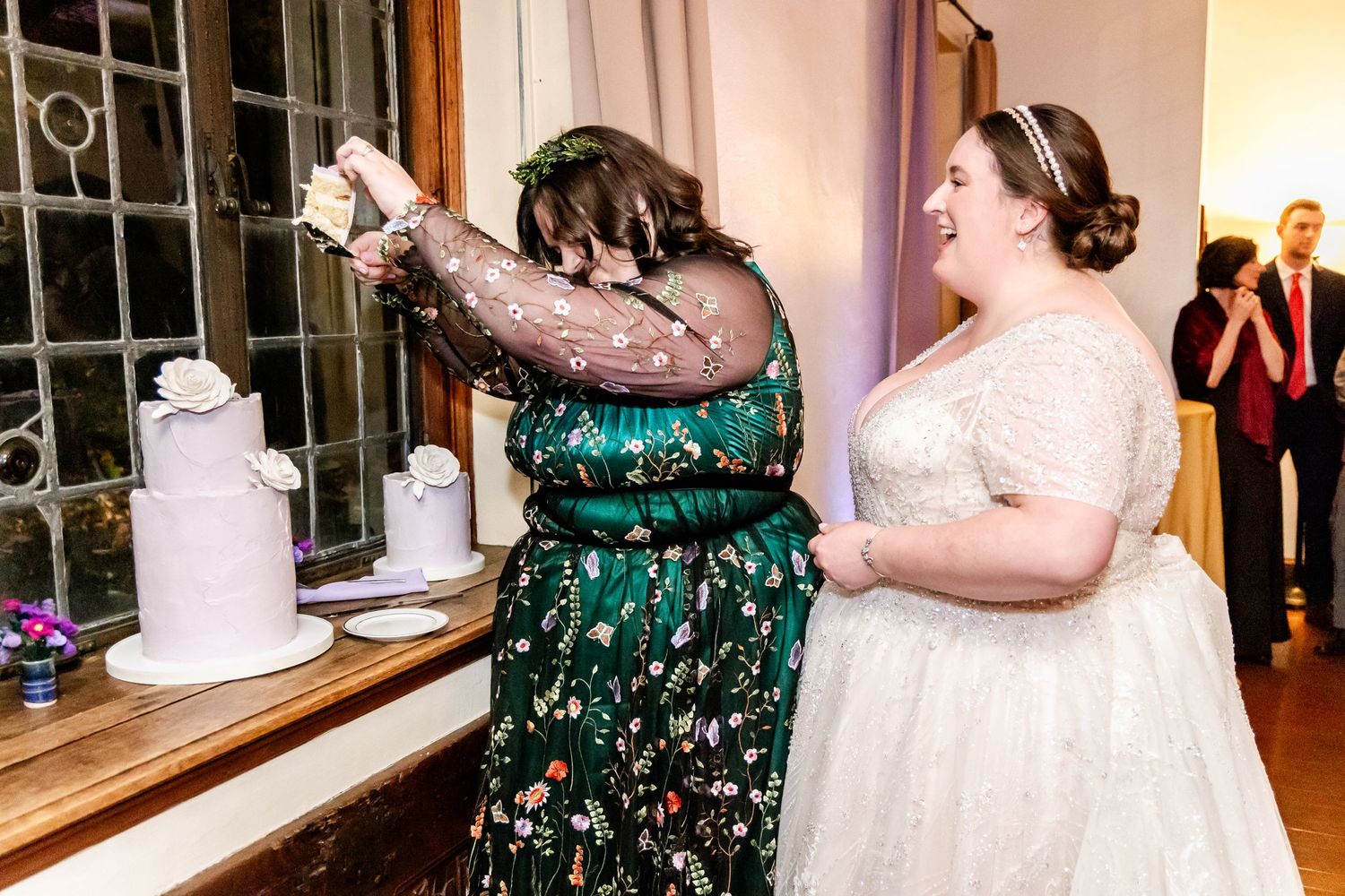 Two wedding guests in elegant dresses share a fun moment near a dessert display.