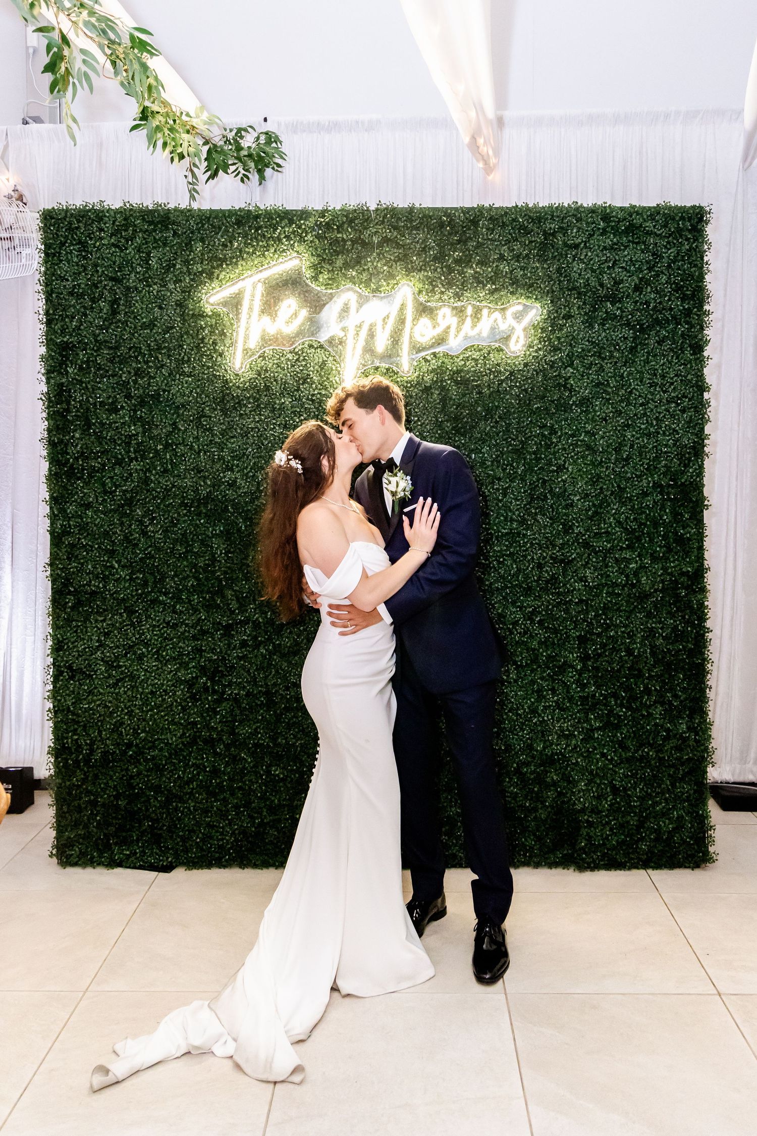 Romantic dance sequence between newlyweds against a green hedge wall with neon lighting.