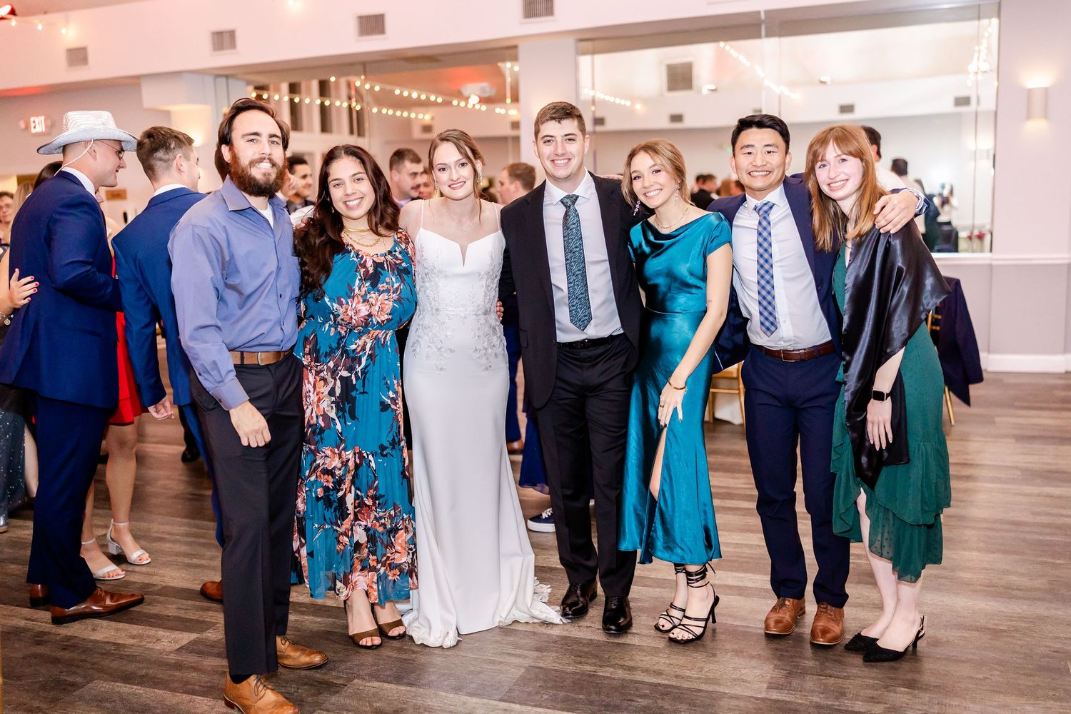 Large group of wedding guests dancing and celebrating in a spacious reception venue.