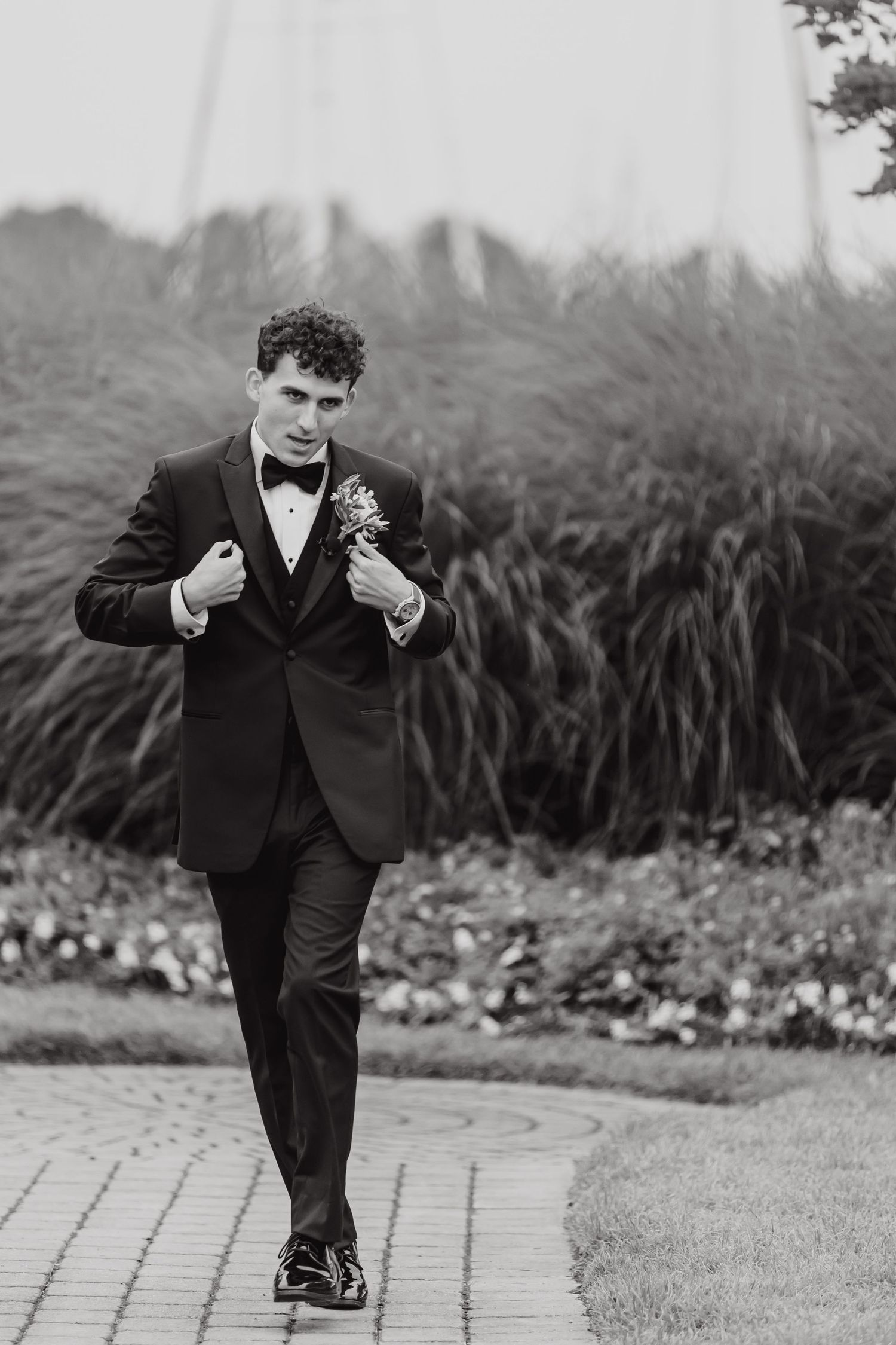 Black and white photo of a groom dancing playfully outdoors in a formal suit.