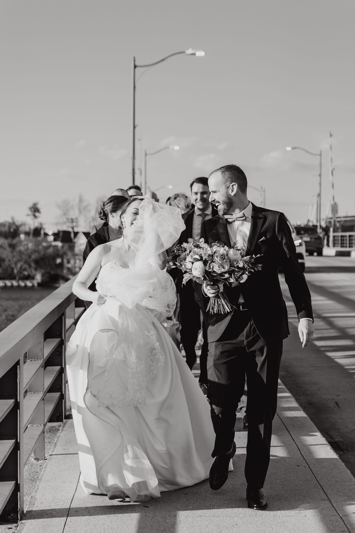 Couple walking on a sunlit boardwalk during their wedding photoshoot with lamp posts in background.