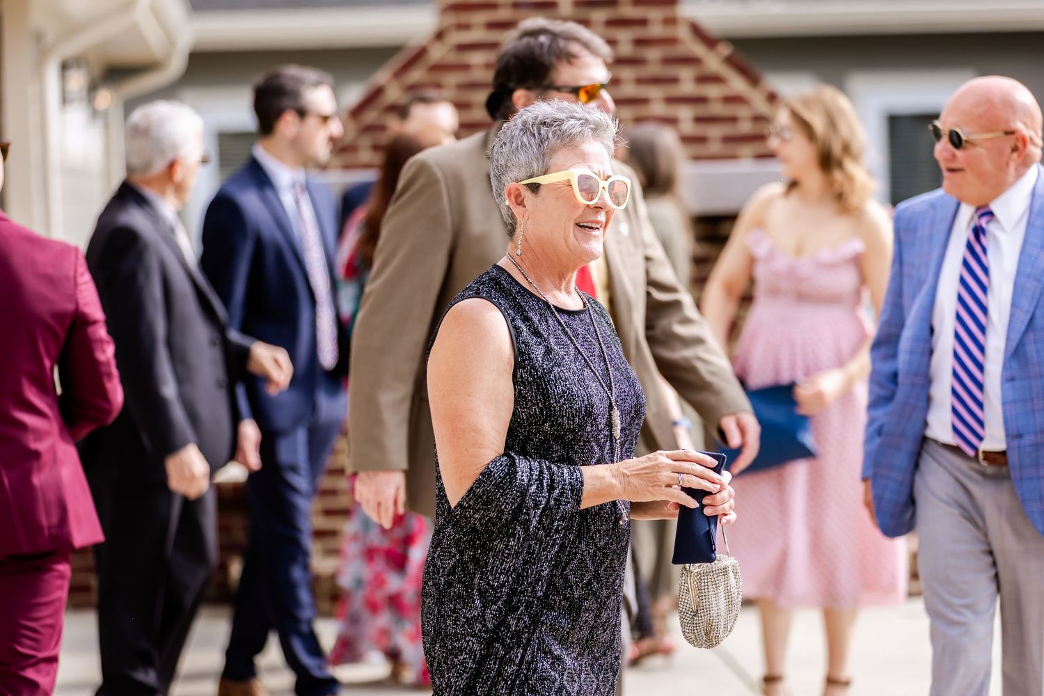 Wedding guests mingle and socialize during an outdoor reception near a brick building.