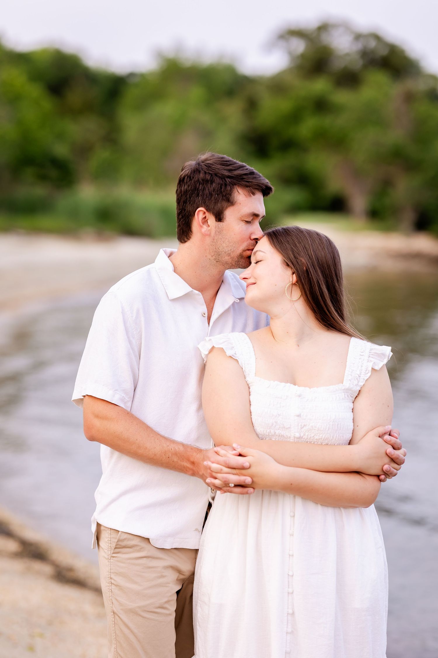 A couple in white and beige embraces on a peaceful beach shoreline during a romantic photoshoot sequence.