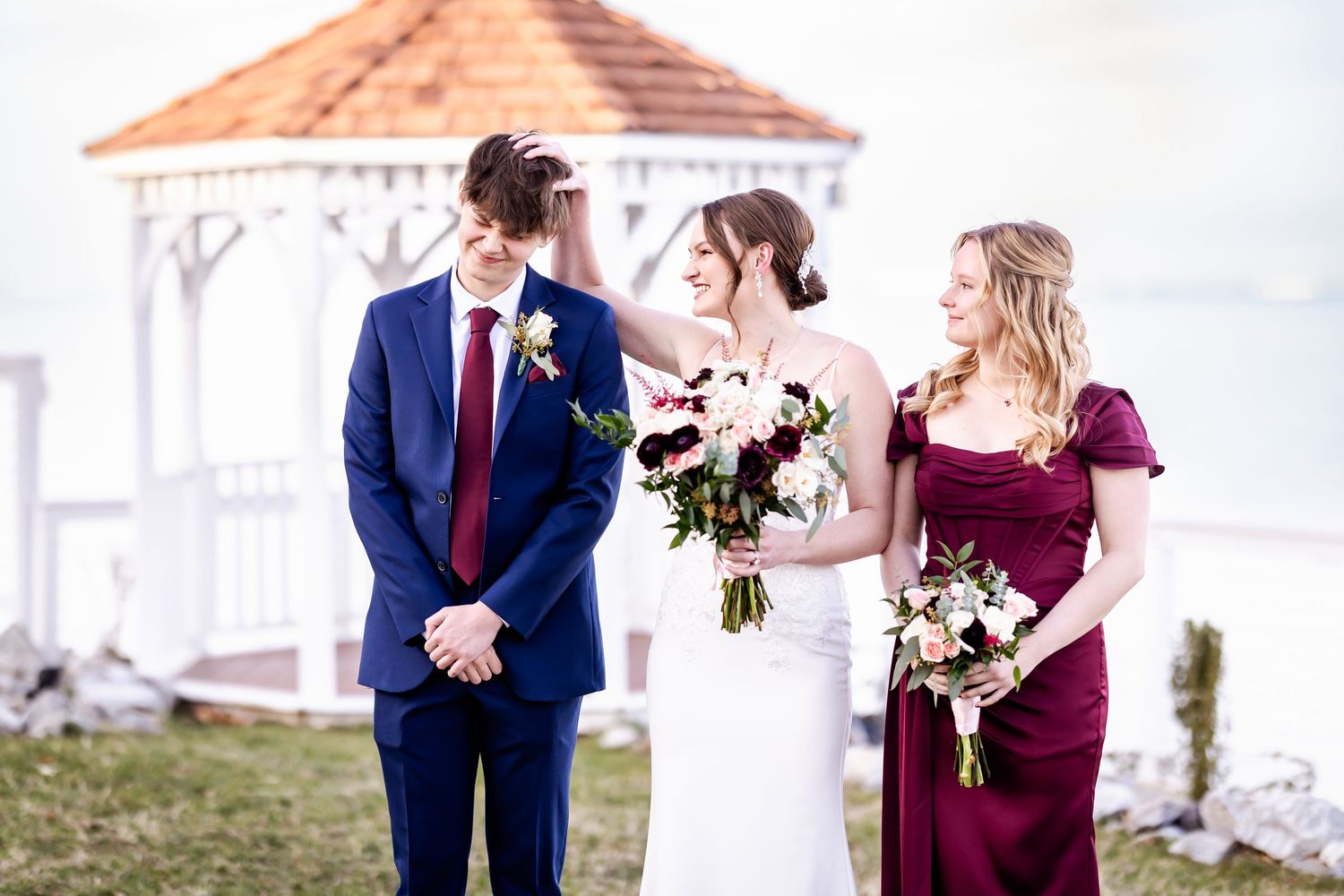 Wedding party in burgundy and navy attire posing outside a white columned building.