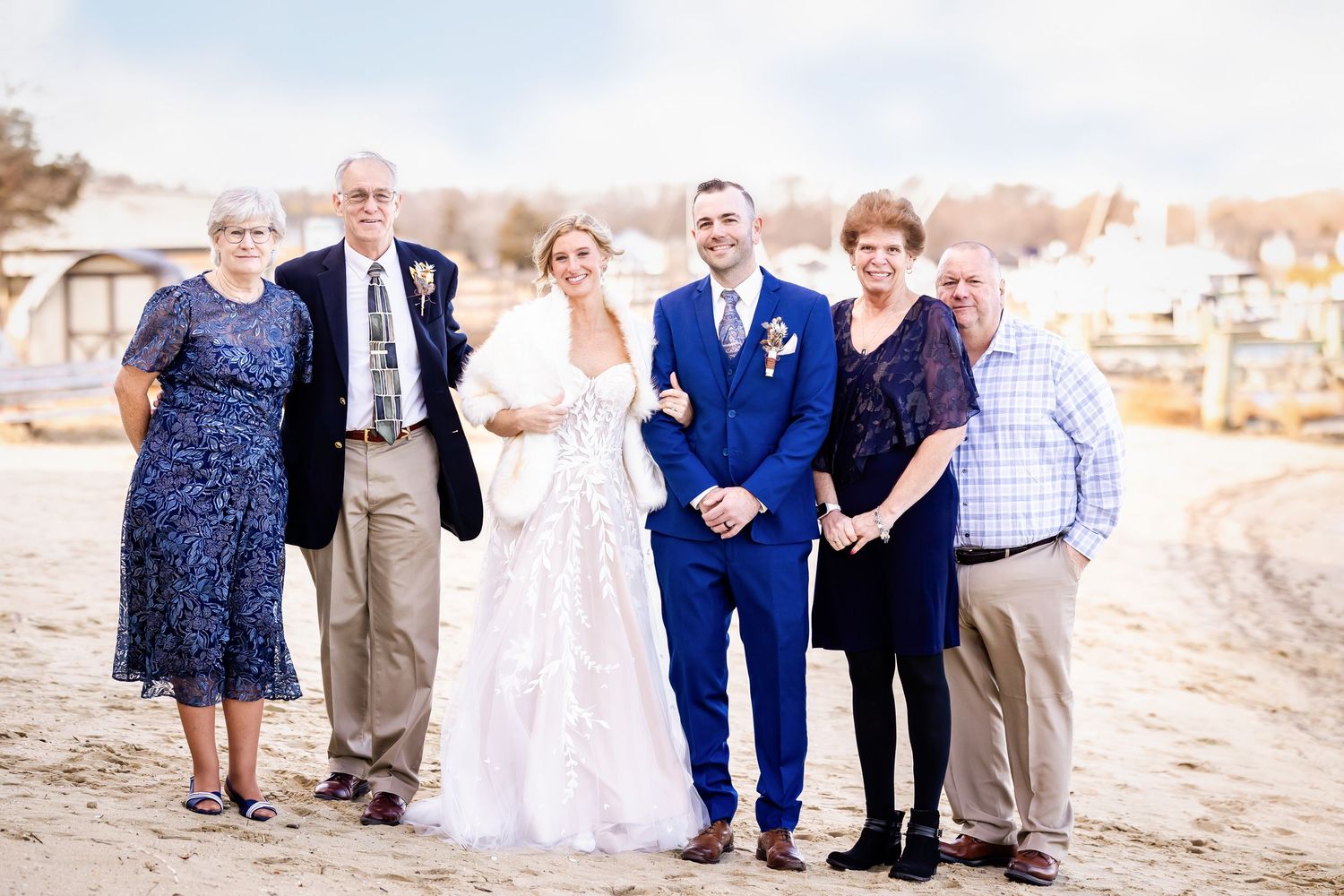 A group of wedding guests and couple pose together on a beach during a wedding celebration.