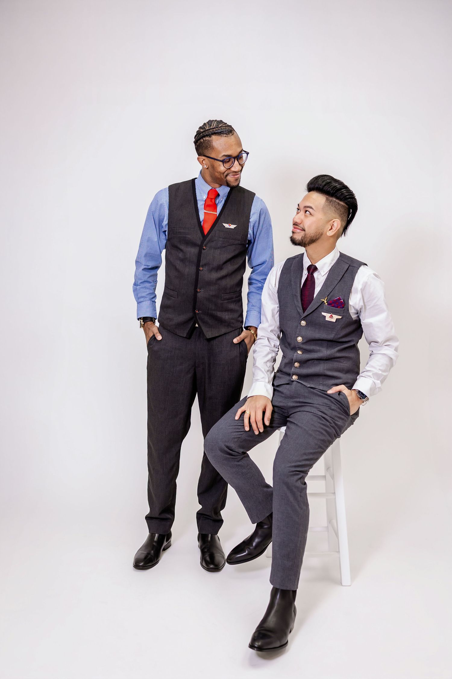 Two men in business casual attire share a candid moment while seated in a studio setting with white backdrop.