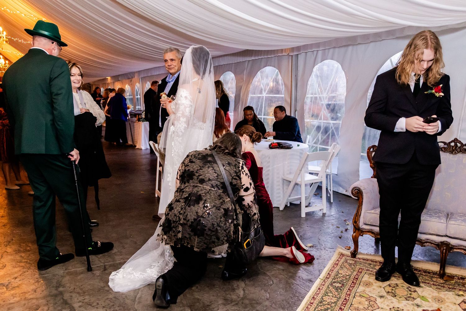 Wedding reception guests gather in a white tent decorated with fabric draping.