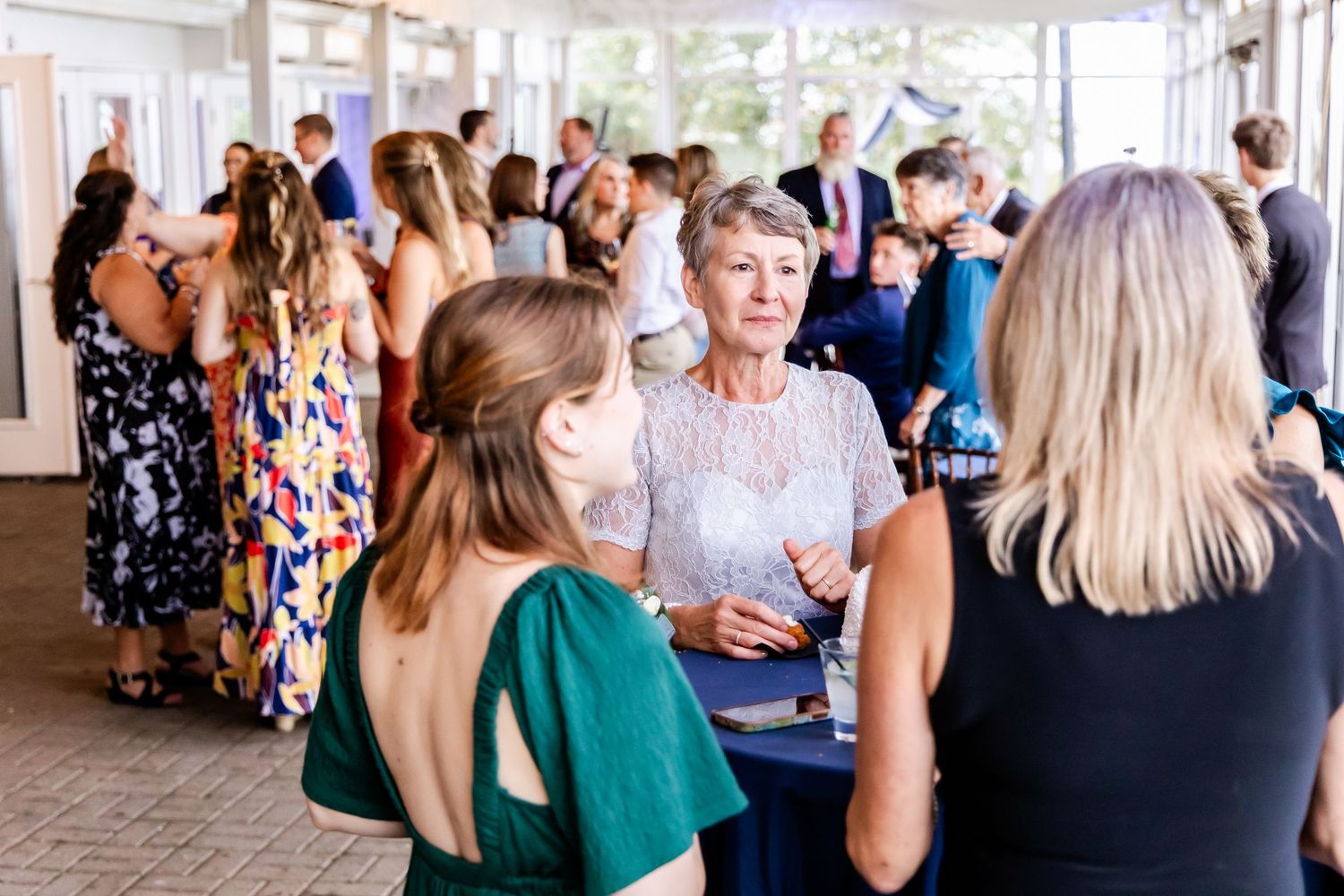Wedding guests mingling and socializing during reception in bright indoor venue.
