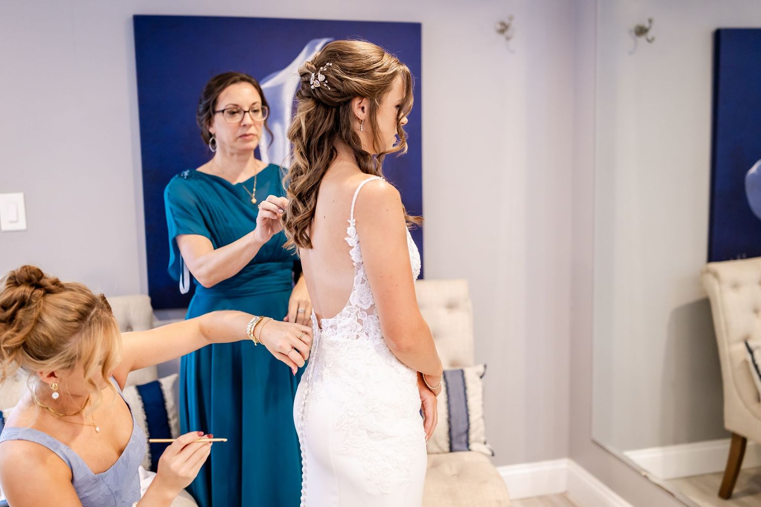 Bride getting ready in a blue-walled room with bridesmaids helping with final preparations.