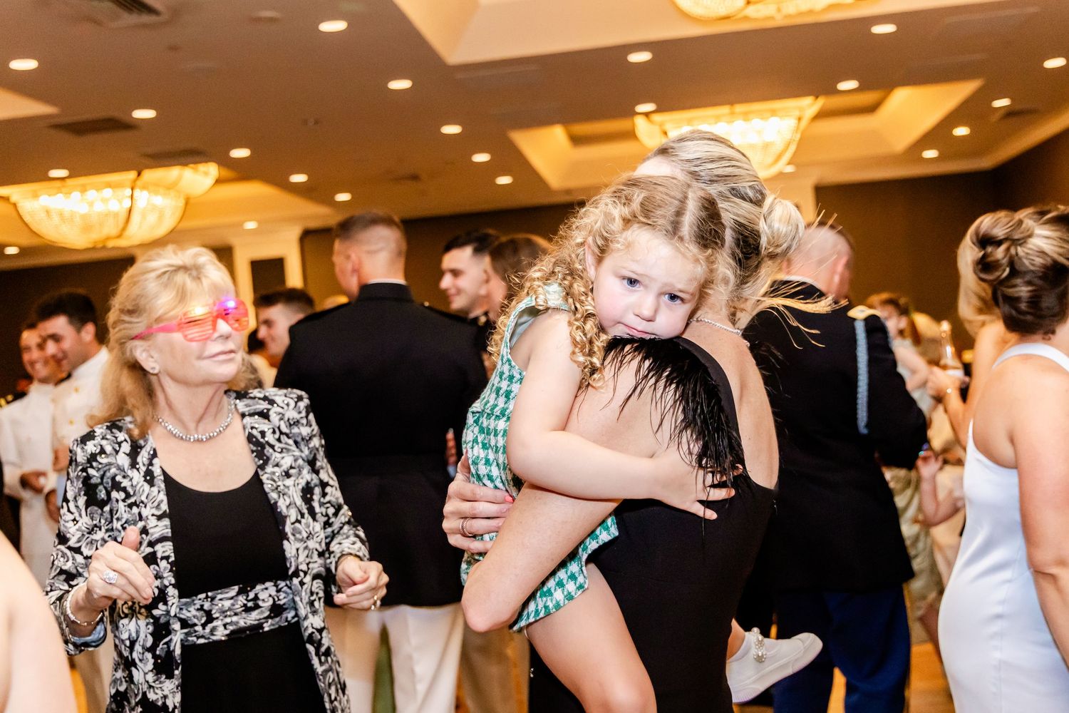Wedding guests dancing and celebrating under ornate chandeliers in a ballroom.