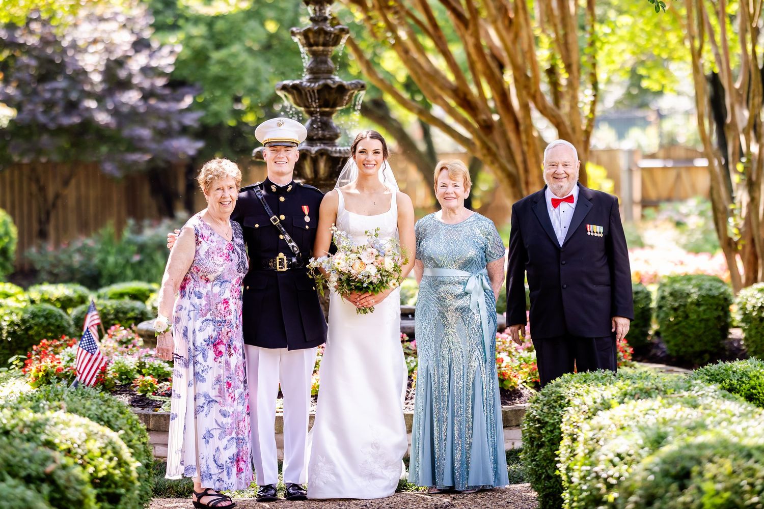 Wedding party poses for group photos in a lush garden setting with blooming trees.