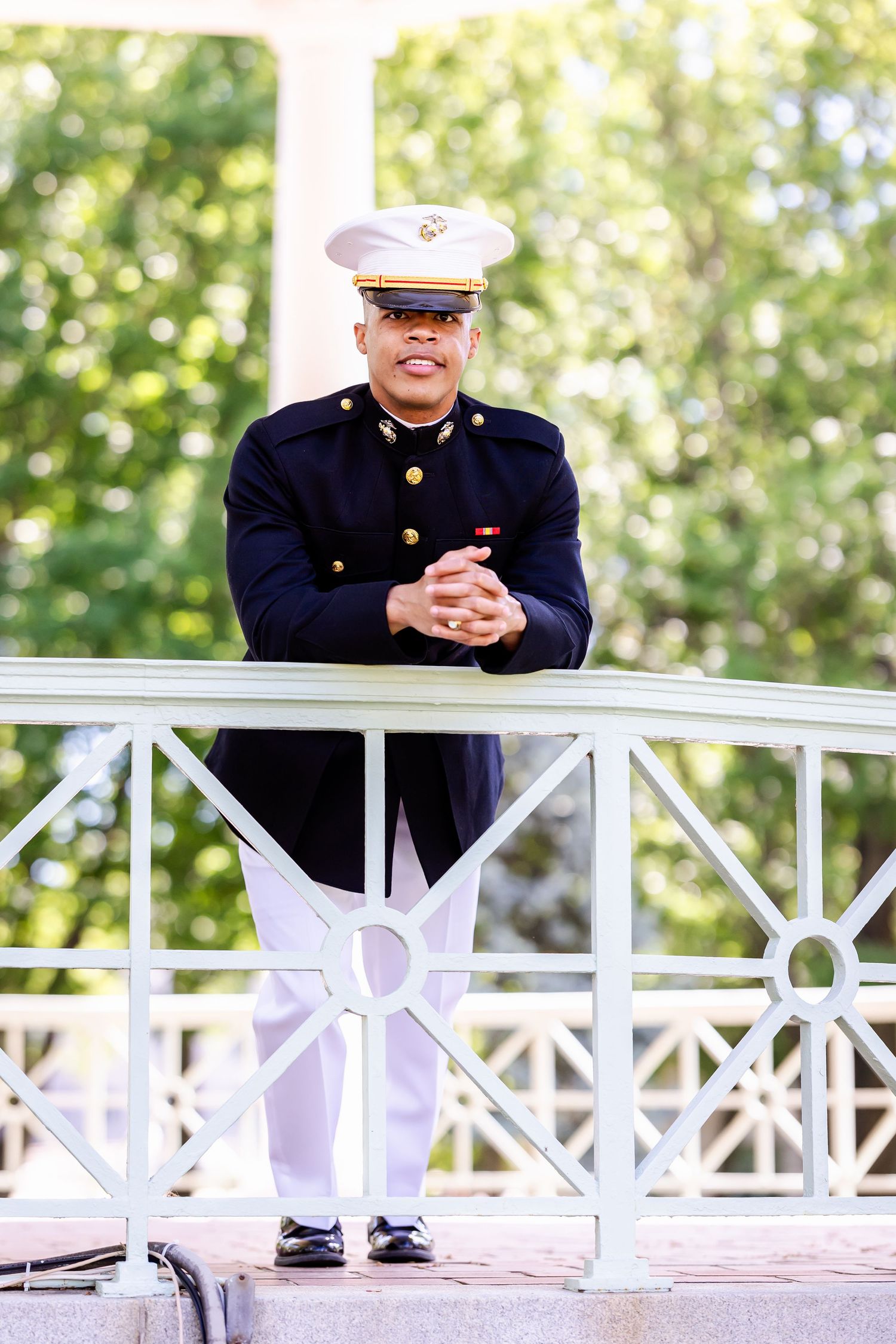 Military service member in dress uniform sitting on outdoor railing.