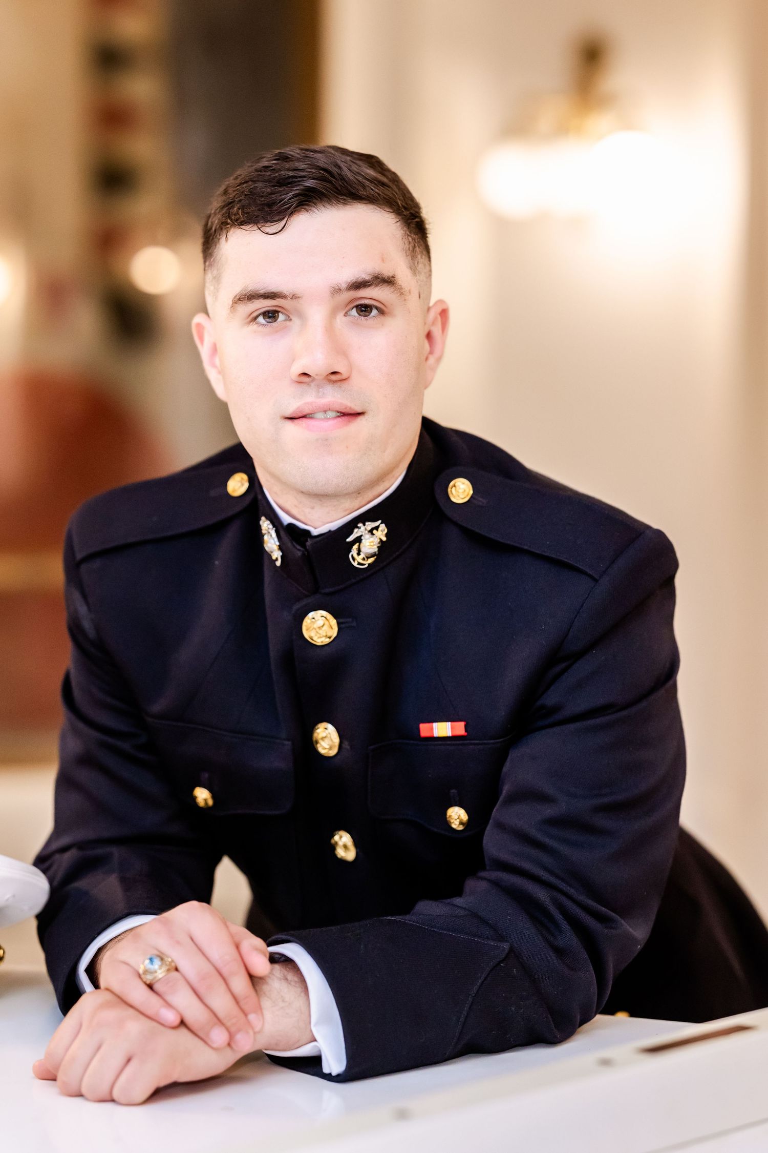 Military service member in formal dress uniform poses indoors for professional portrait.