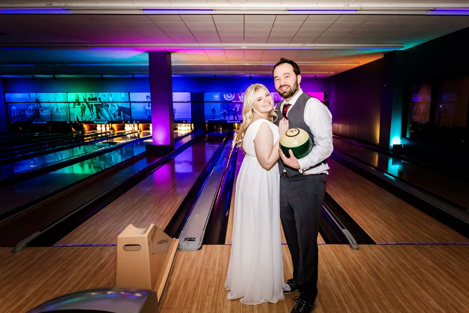 A wedding celebration at a bowling alley with colorful neon lights illuminating the lanes and festive atmosphere.