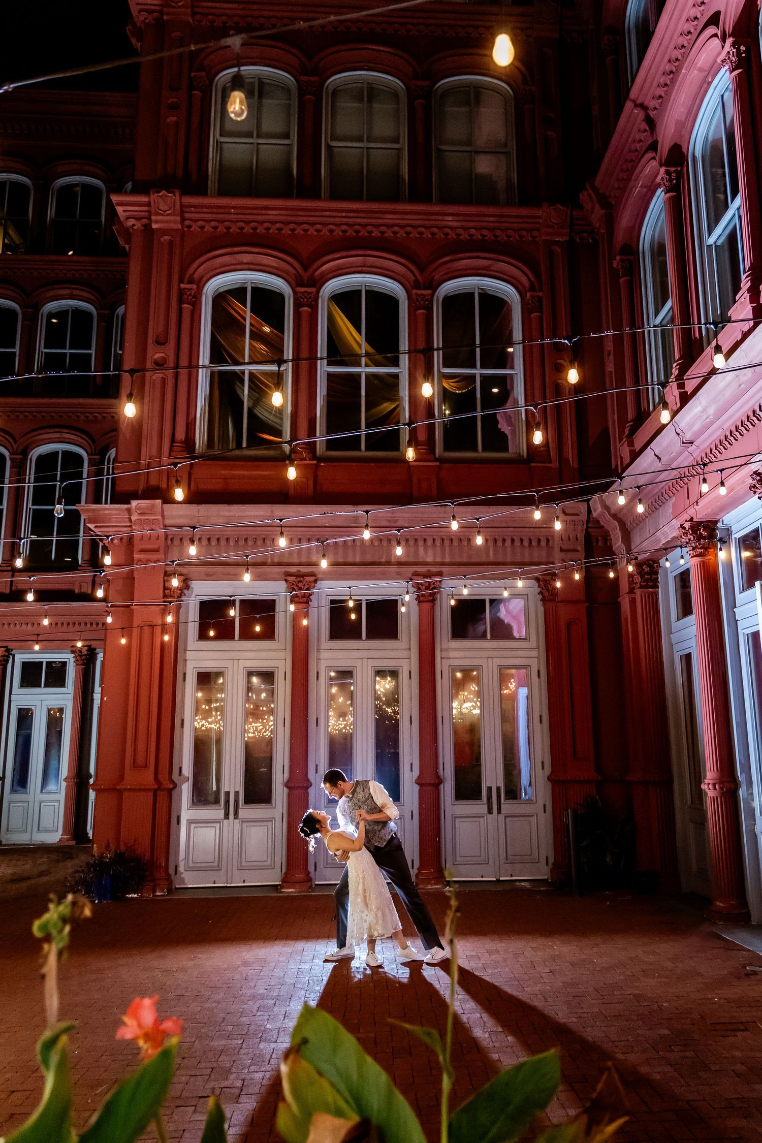 Historic theater lobby illuminated in pink lighting with ornate architectural details and hanging pendant lights.