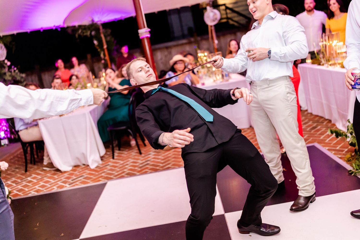 Guests dancing and having fun at a wedding reception with purple lighting.
