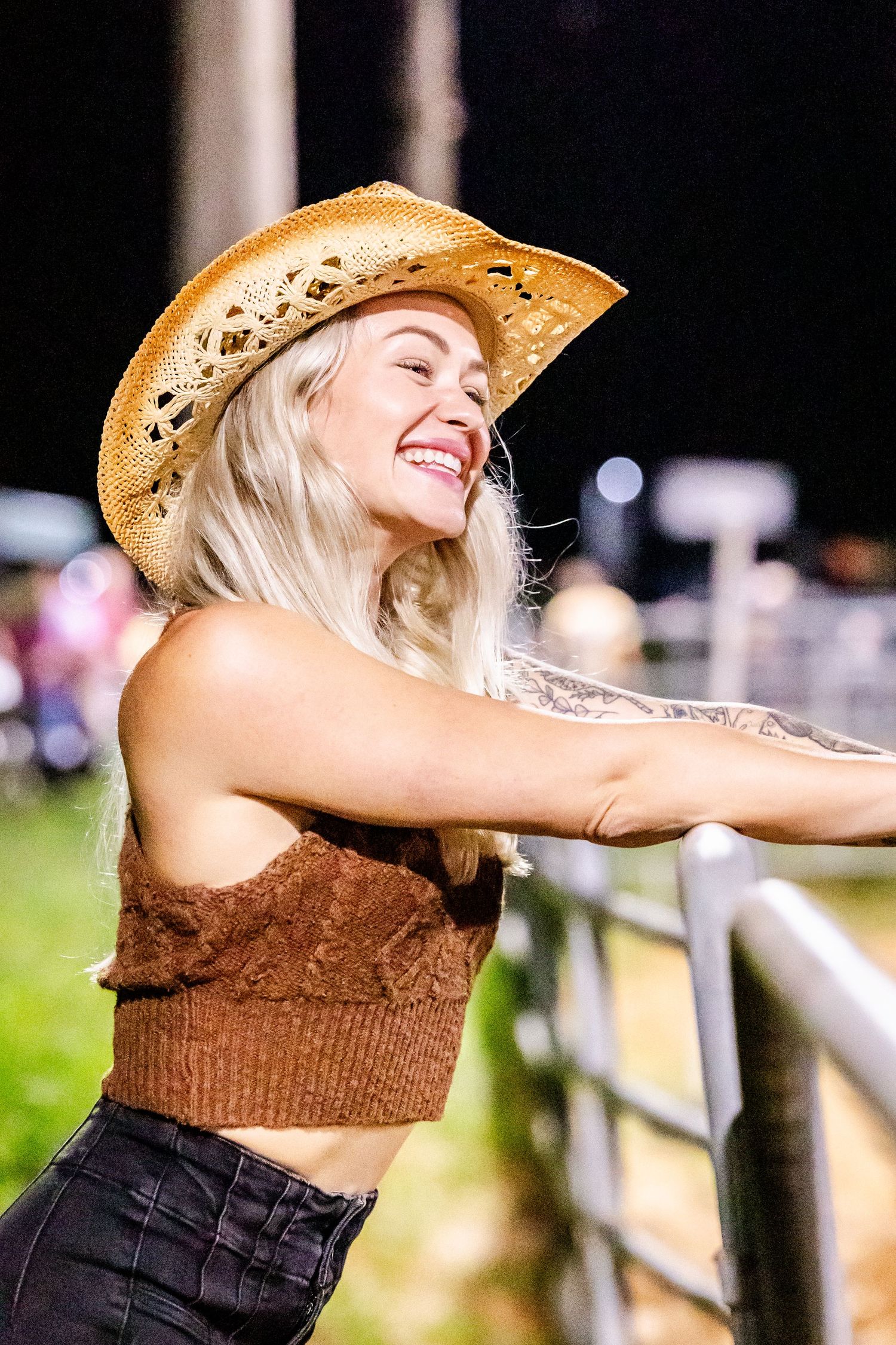 Person in straw hat and black top dances joyfully outdoors while wearing western-style clothing.