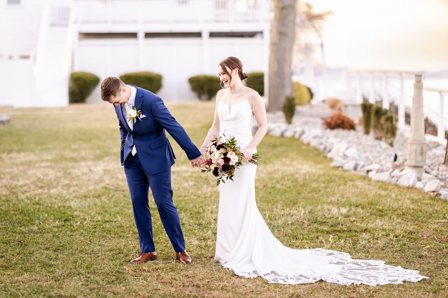 Wedding couple walks together on grassy hill with bride's long train trailing behind.