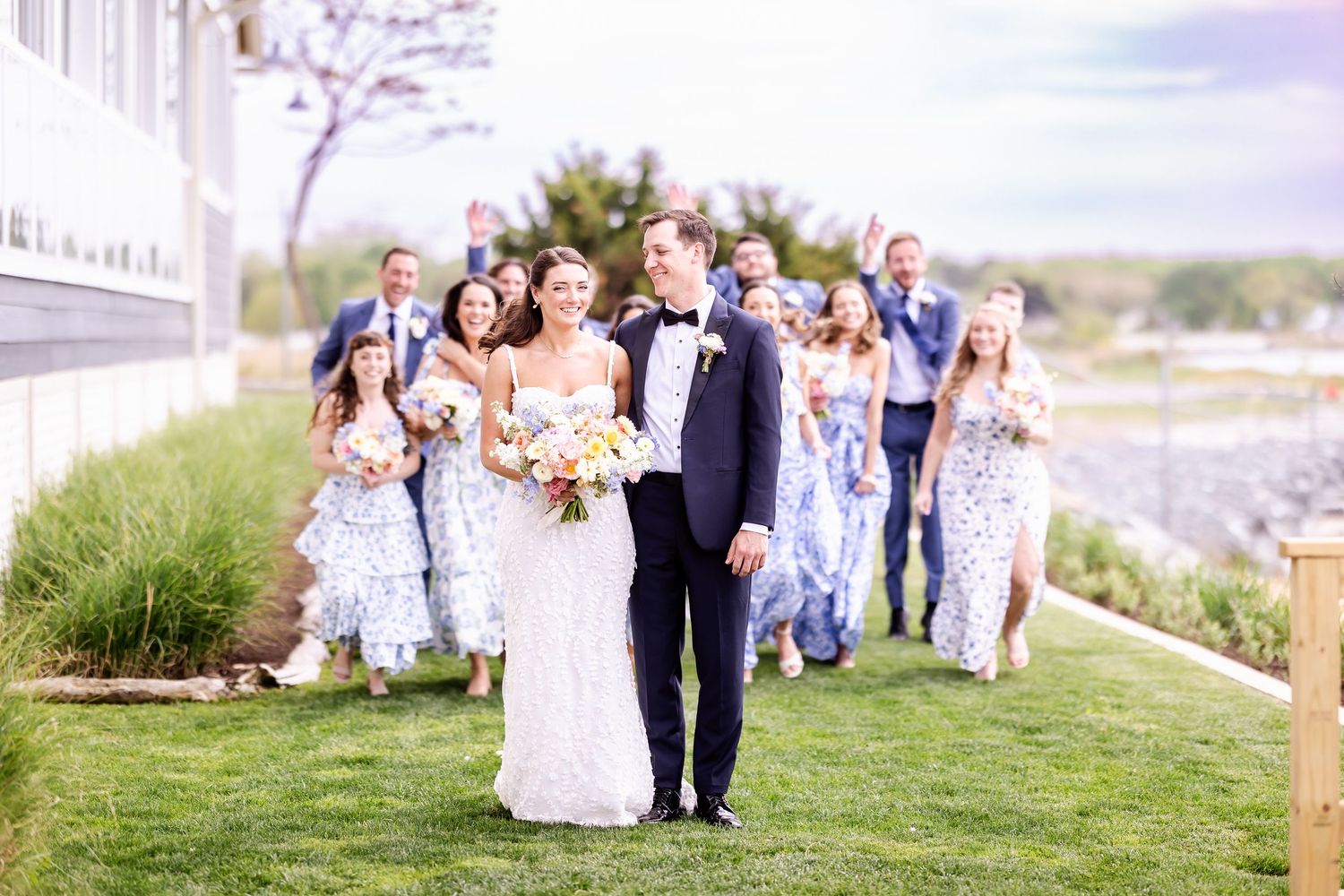 Wedding party poses together on grassy hillside overlooking scenic coastal view.