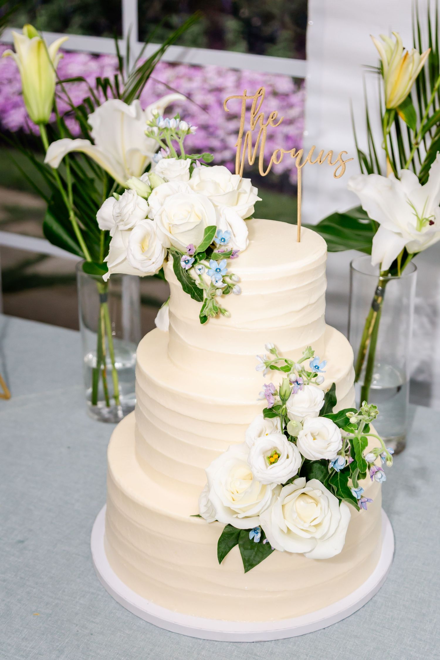 Three-tiered white wedding cake decorated with fresh roses and greenery.