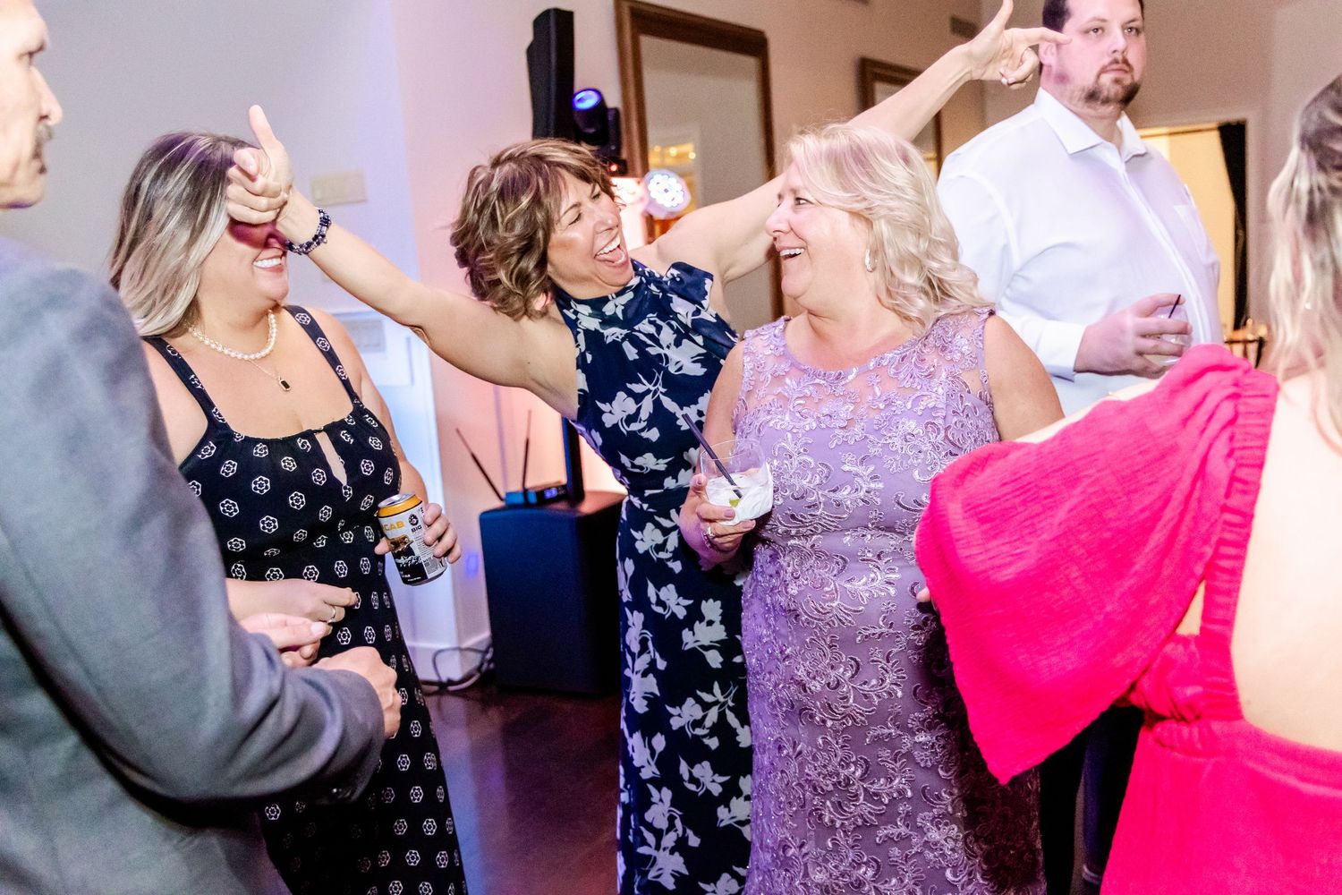 Wedding guests dancing and celebrating at an indoor reception venue with colorful lighting.