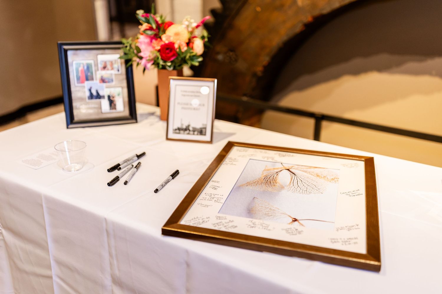 Wedding reception guest book table with framed photos and floral arrangements.