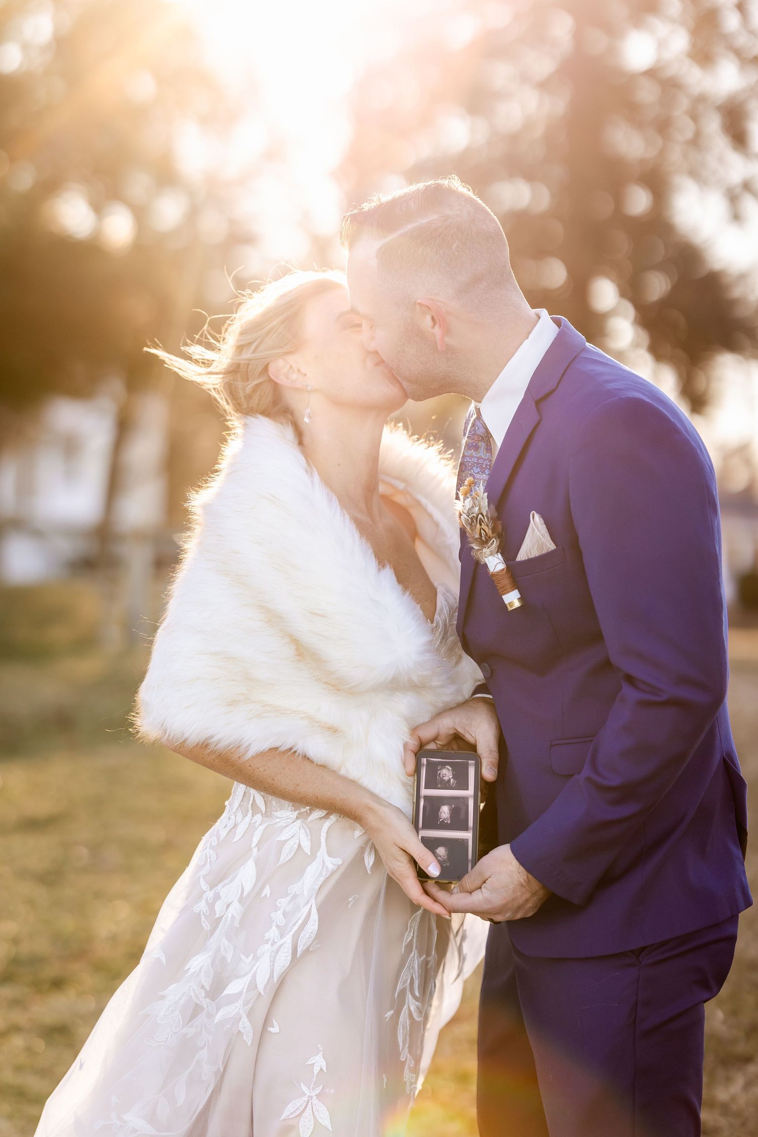 Romantic sunset moment captured as couple share an intimate kiss in winter wedding attire.