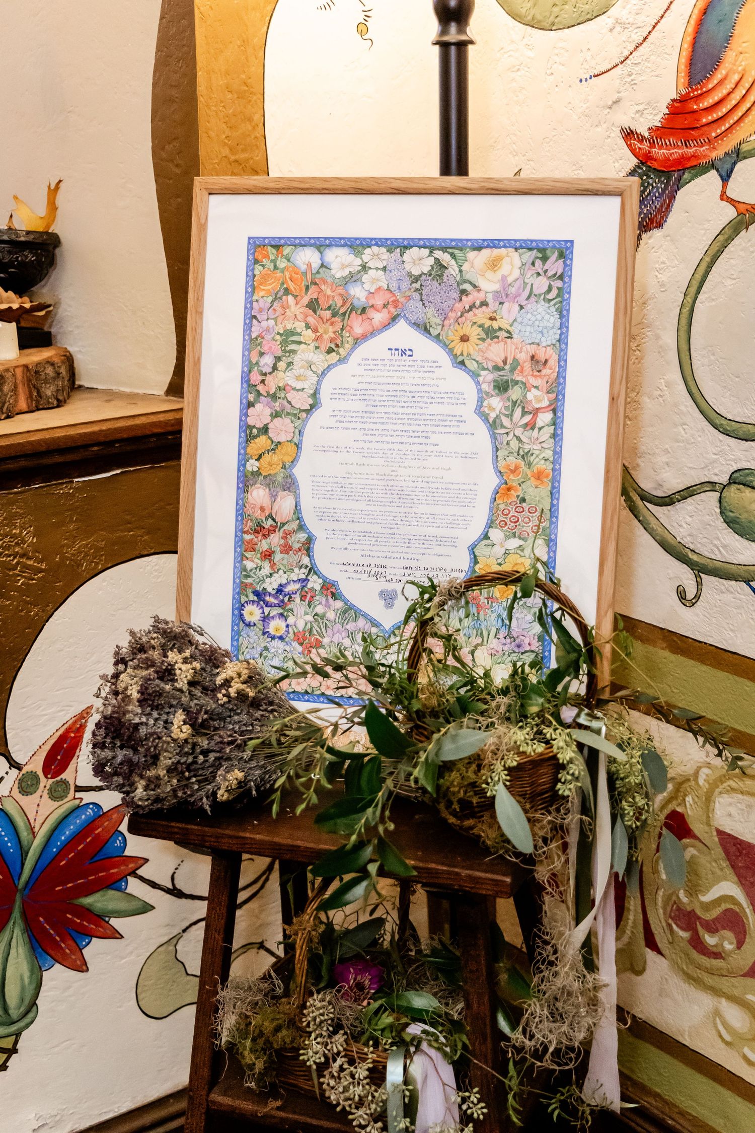 A framed document with floral border decoration displayed with dried flowers and decorative elements.
