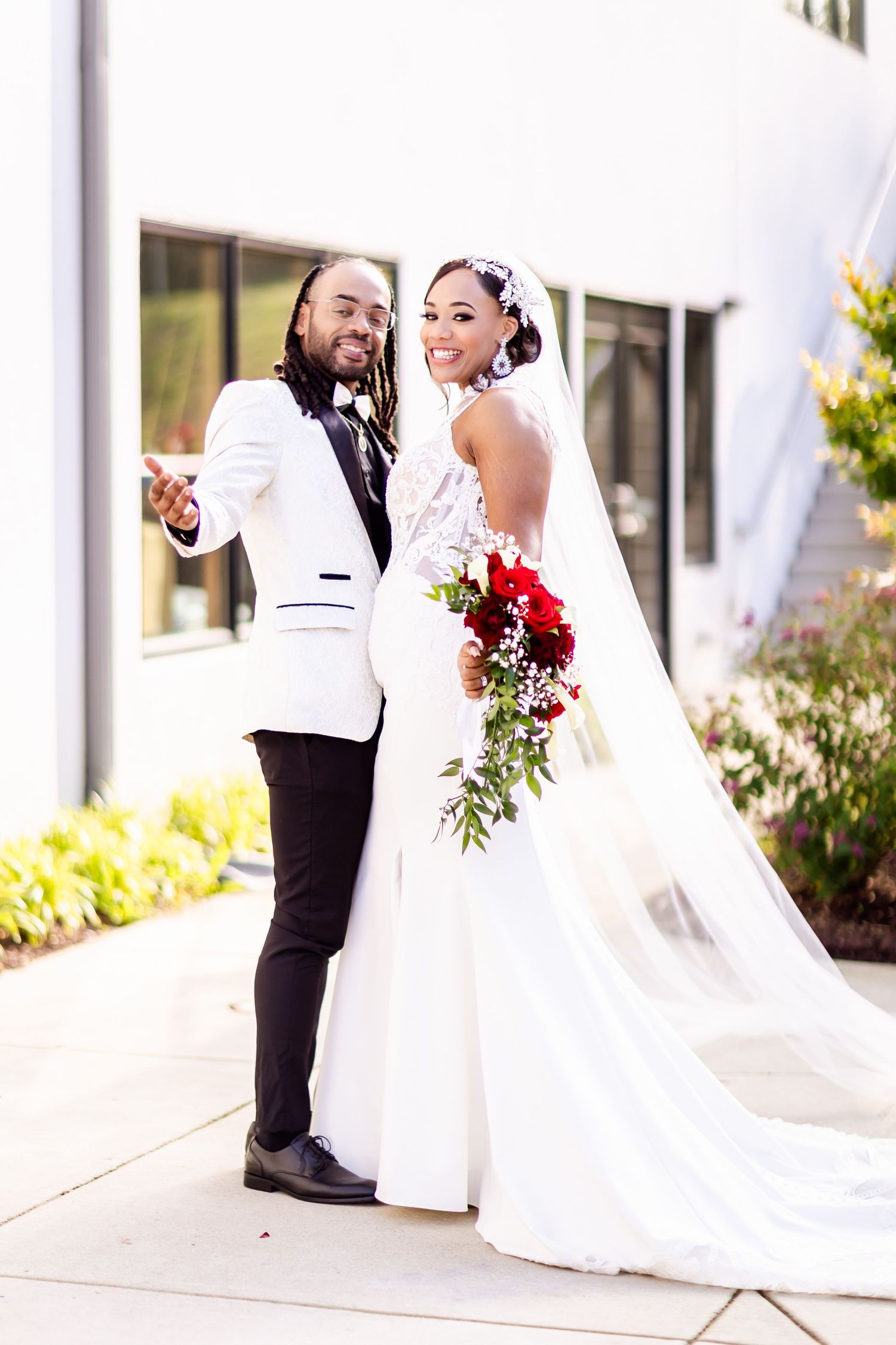 A happy bride and groom posing together outside against a modern white building.