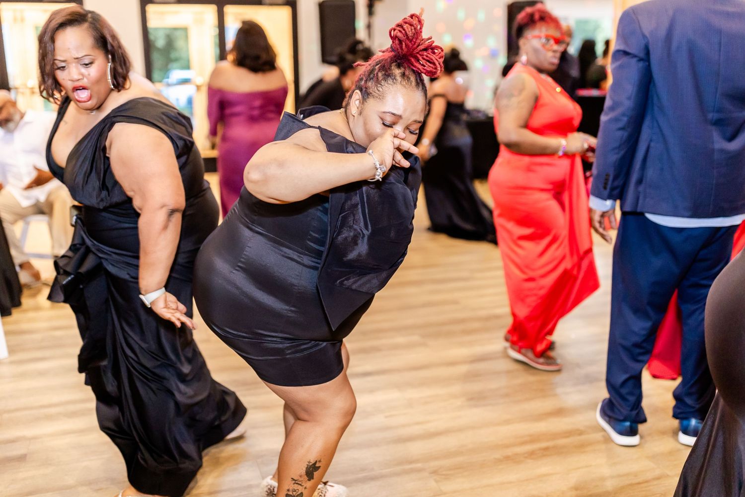 Dancers enjoying themselves on a wooden dance floor at an indoor celebration.