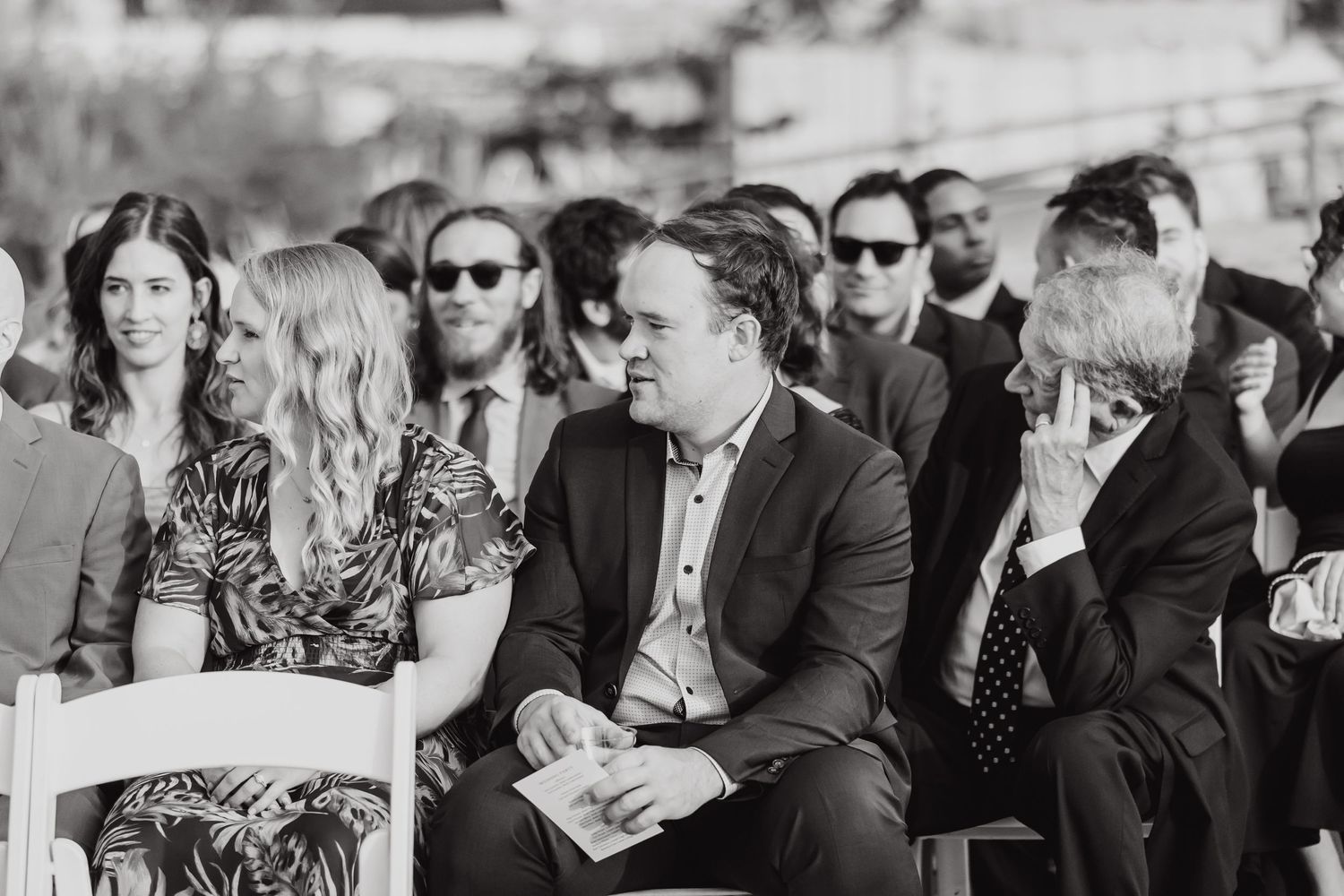 Black and white photo of wedding guests seated in rows during outdoor ceremony.